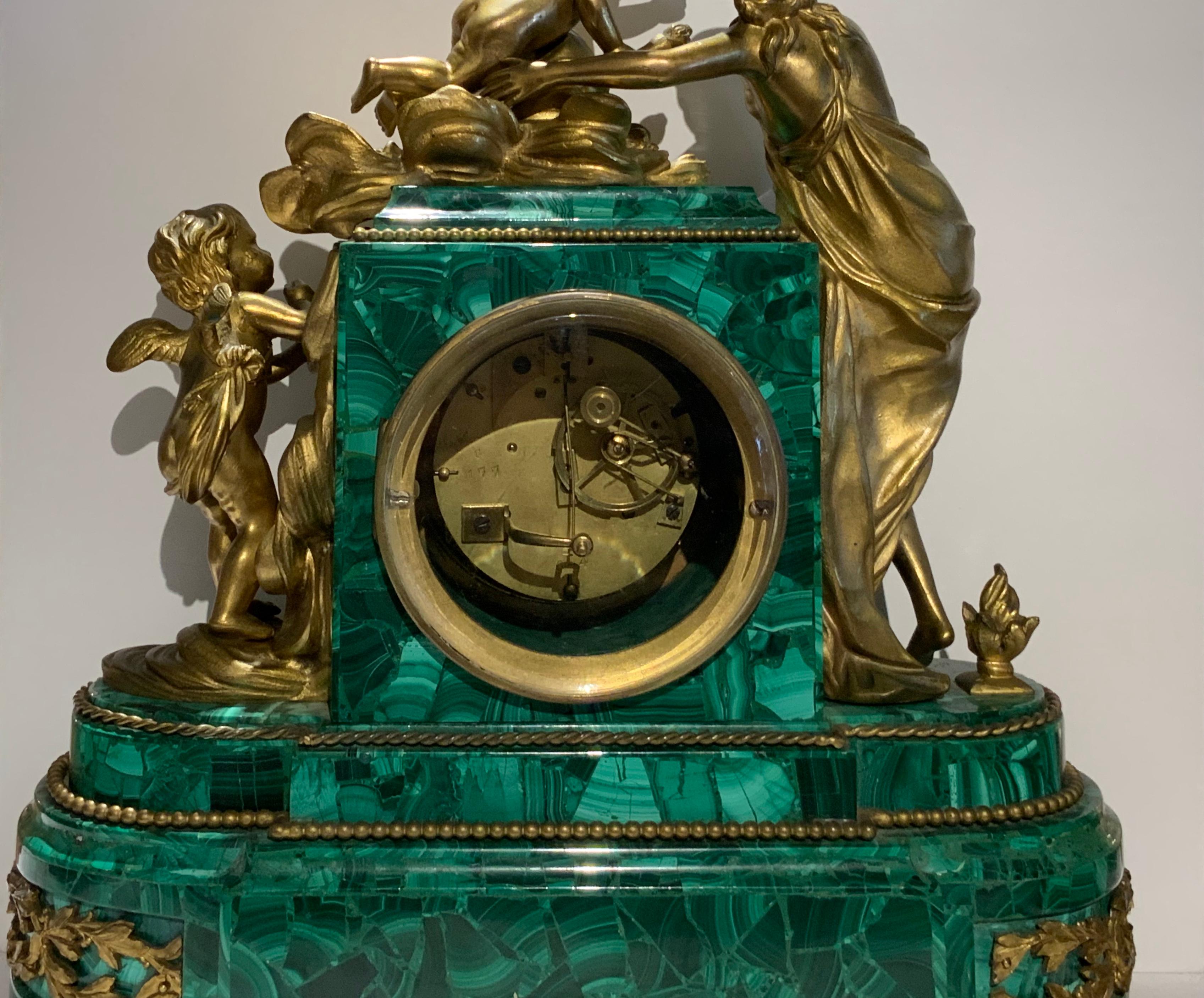 This mantel clock depicts a mythological group scene in bronze of figures representing a cupid with a torch in his right hand in clouds made of scrolls and foliage flirting with a semi nude Venus while another cupid is observing them. The clock case