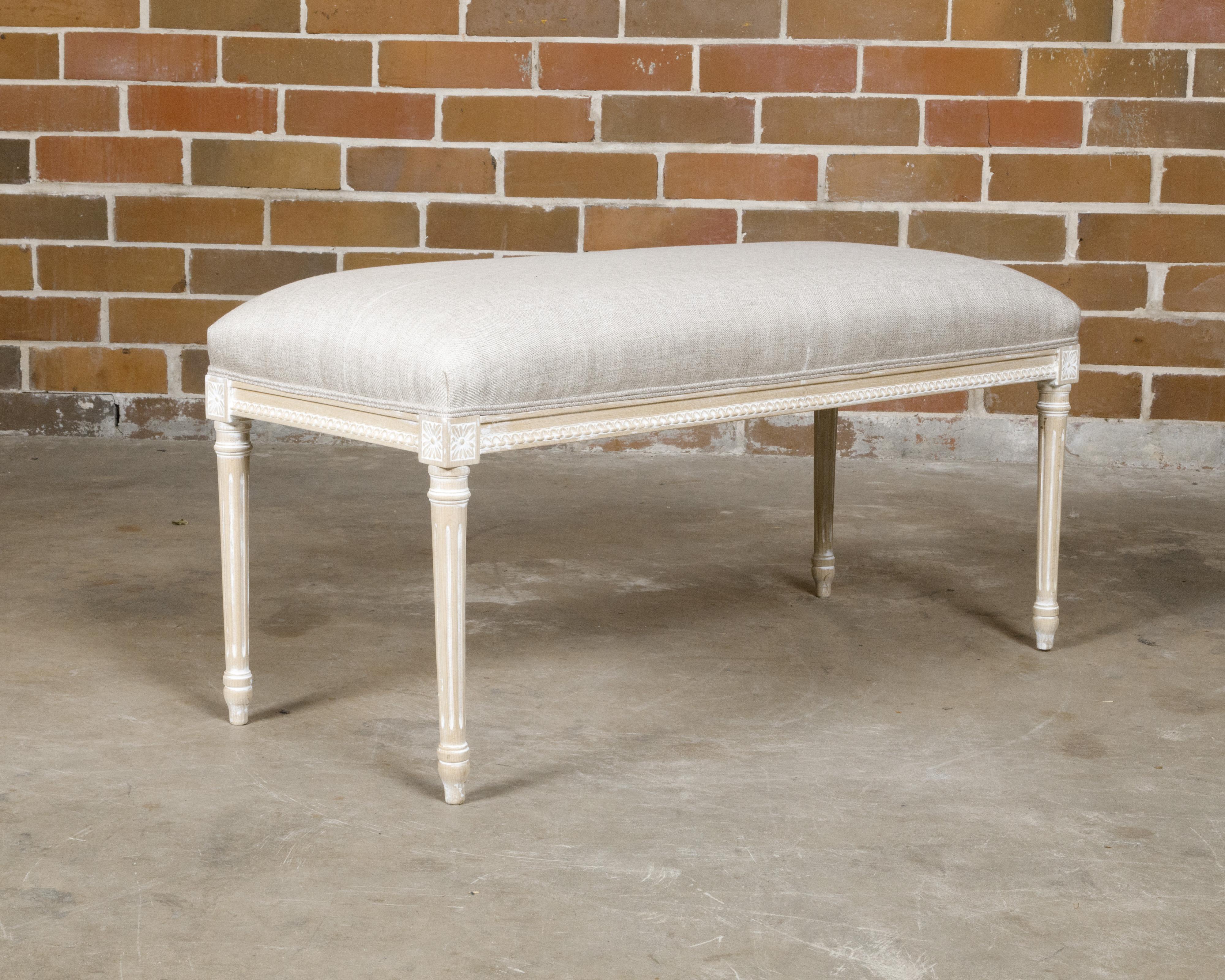 A French Louis XVI style natural wood bench from circa 1900 with white painted accents, carved décor, fluted legs and upholstered seat. This French Louis XVI style natural wood bench from circa 1900 captures the timeless elegance of classic French