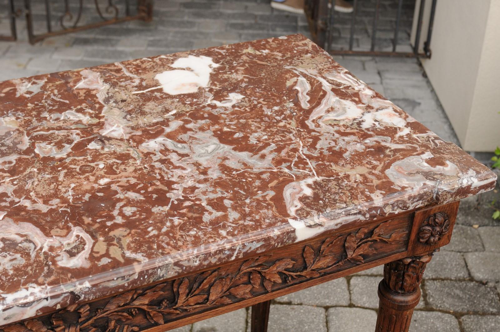 A French Louis XVI style carved oak console table from the late 19th century, with red marble top and fluted legs. Born at the end of the reign of France's last emperor Napoleon III, this console table presents the stylistic characteristics of the