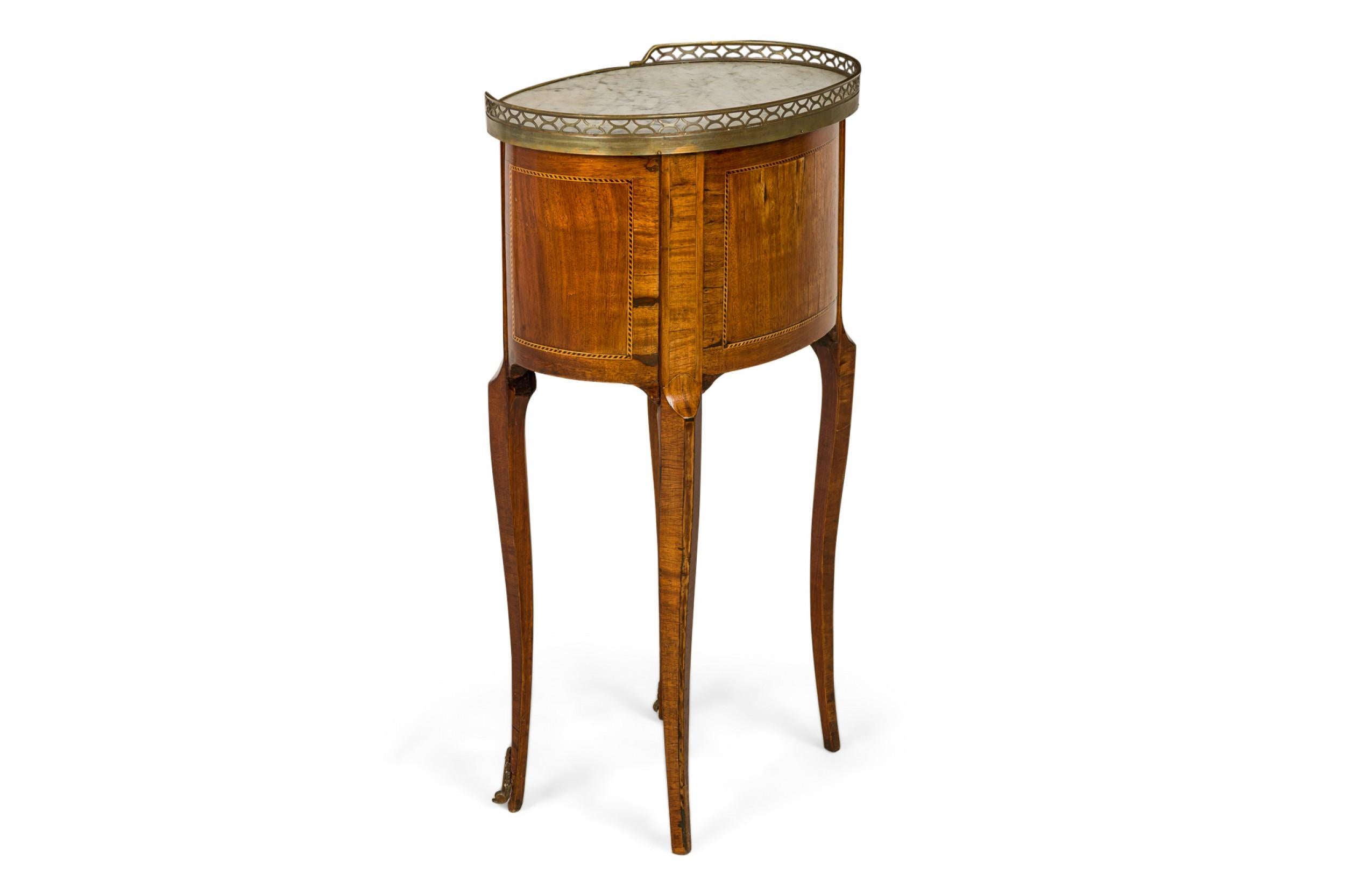 French Louis XVI-style (19/20th Century) oval mahogany bedside / end table with three shallow drawers below a white marble top with partial bronze gallery, resting on four gently curved legs ending in bronze sabots.

Condition: Good; Wear consistent