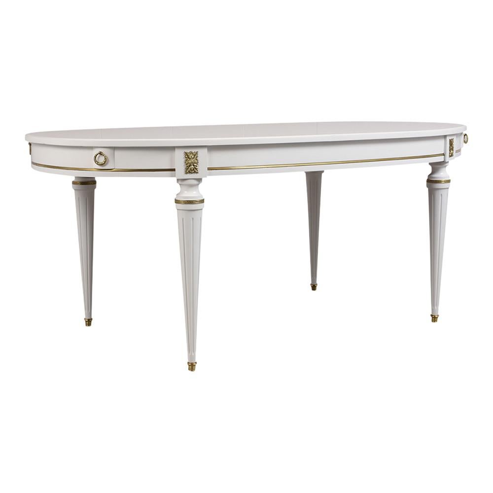 This Louis XVI style oval dining table is made out of mahogany wood and has been stained in white color with a lacquered finish. It also features brass moldings and accents around the top corners and carved legs. The Vintage 1950's Dining Table is