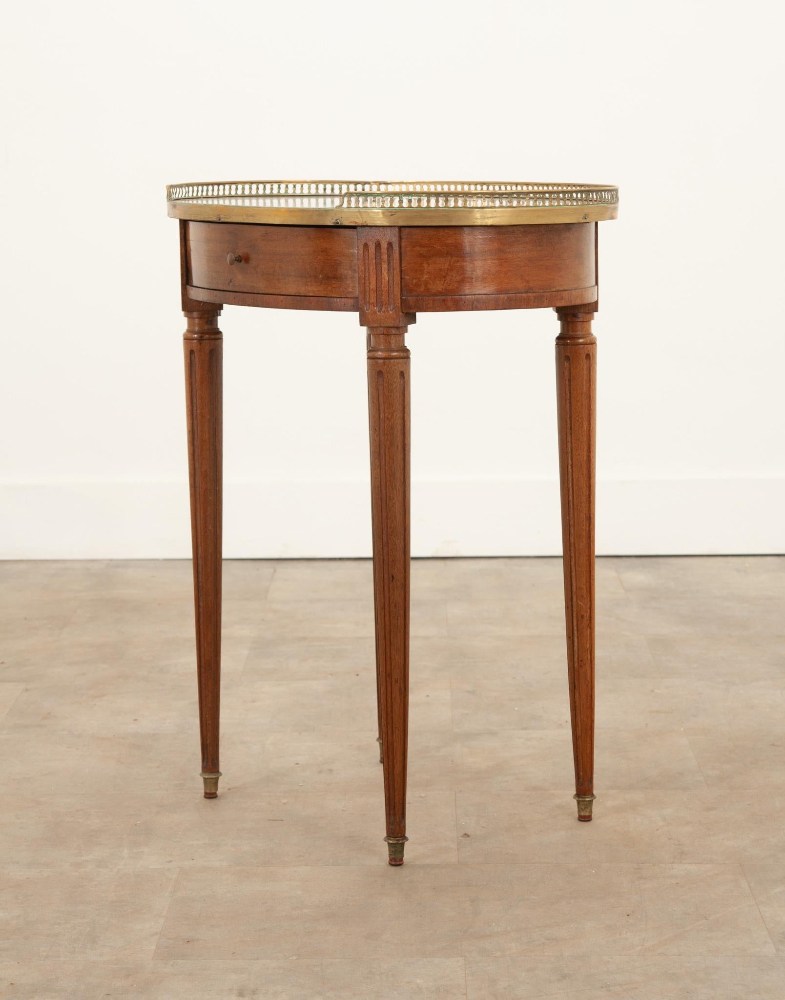 This no- nonsense mahogany table is a fantastic addition to any space. Topped with an inset piece of antique white marble that’s surrounded by a 3/4th pierced brass gallery. The apron is finished on all sides and houses a single drawer with a tiny