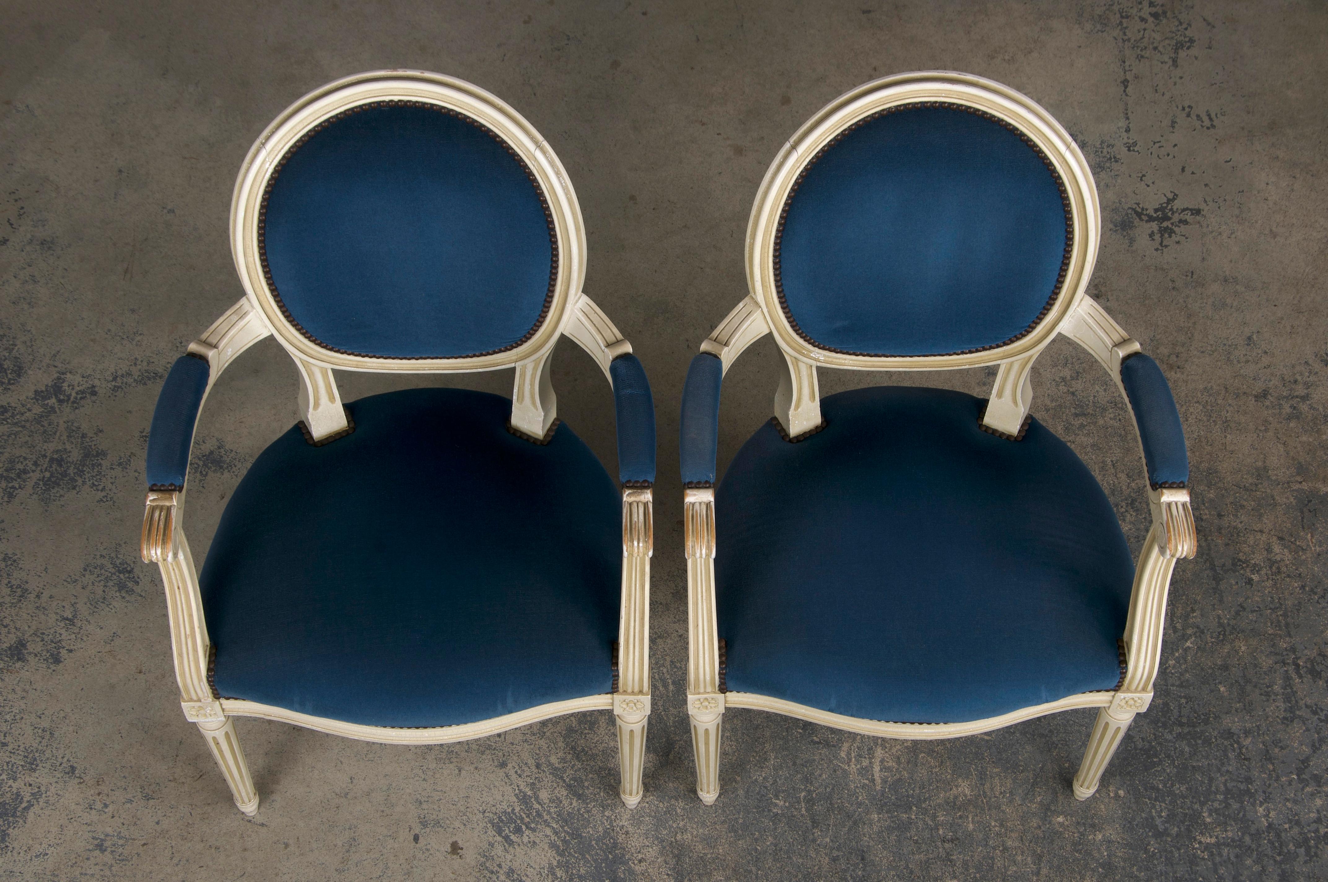 A lovely pair of French armchairs made in the style of Louis XVI, sourced from Provence, France. Each chair features a hand-molded frame adorned with an oval-shaped medallion back. Finished in creamy, antique white lacquer showcasing a naturally