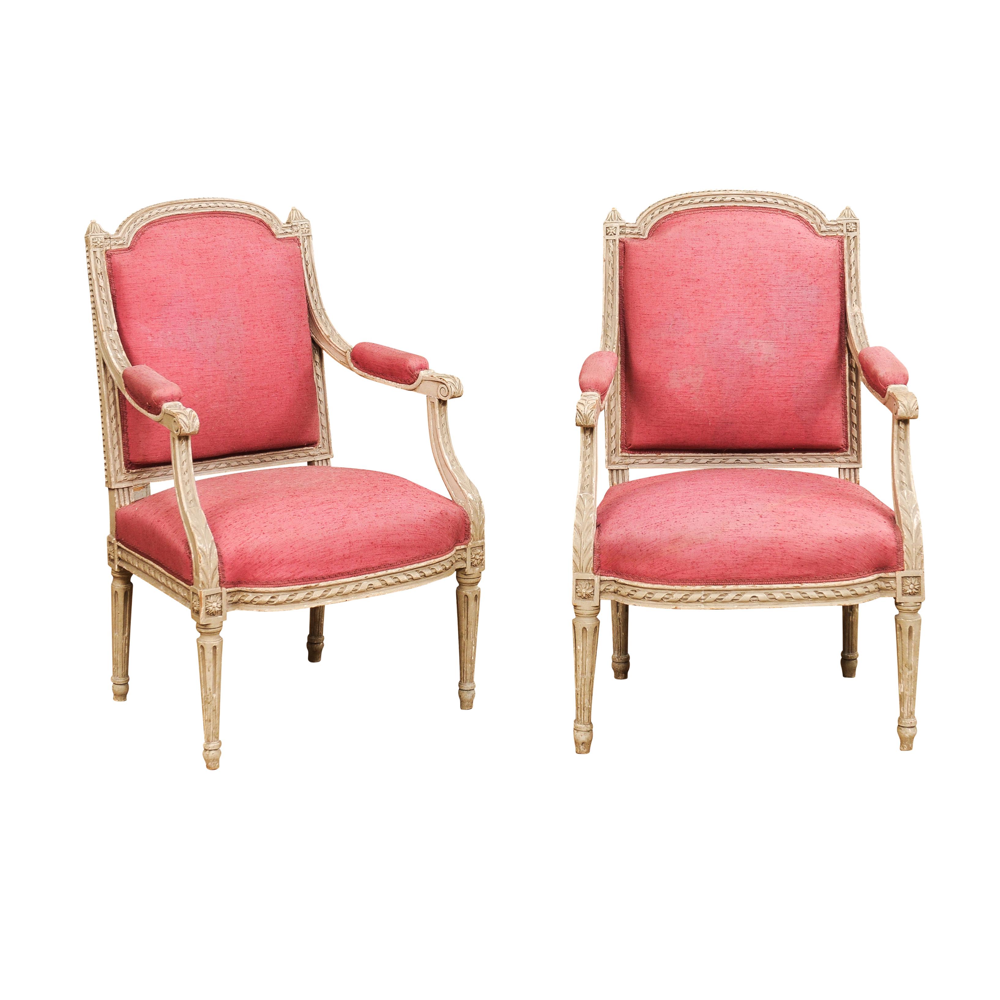 Two French Louis XVI style painted wood armchairs from the 19th century with carved décor including twisted rope motifs, acanthus leaves, rosettes and petite beads. These French Louis XVI style painted wood armchairs from the 19th century are an