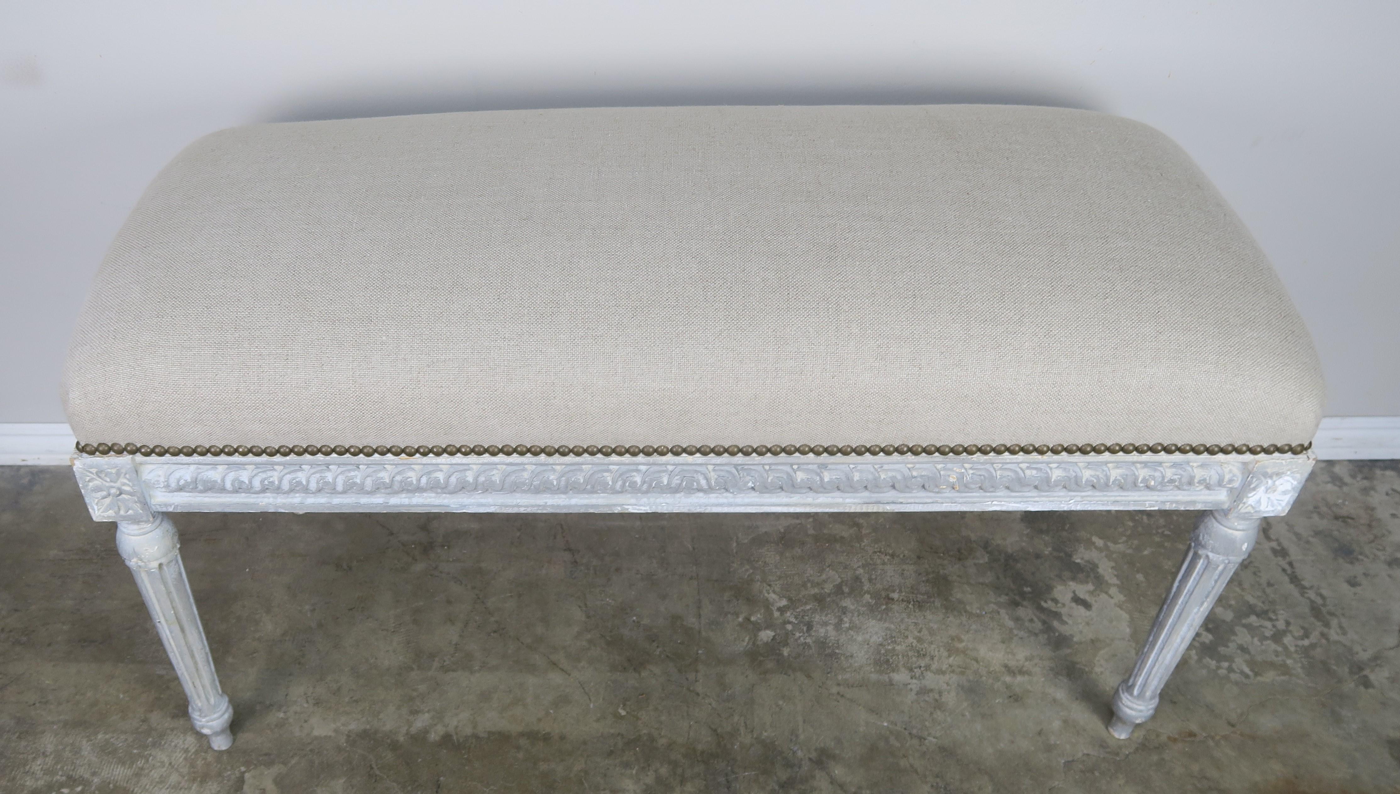 French Louis XVI style painted gray colored bench newly upholstered in a washed Belgium linen and detailed with antique brass nailhead trim.