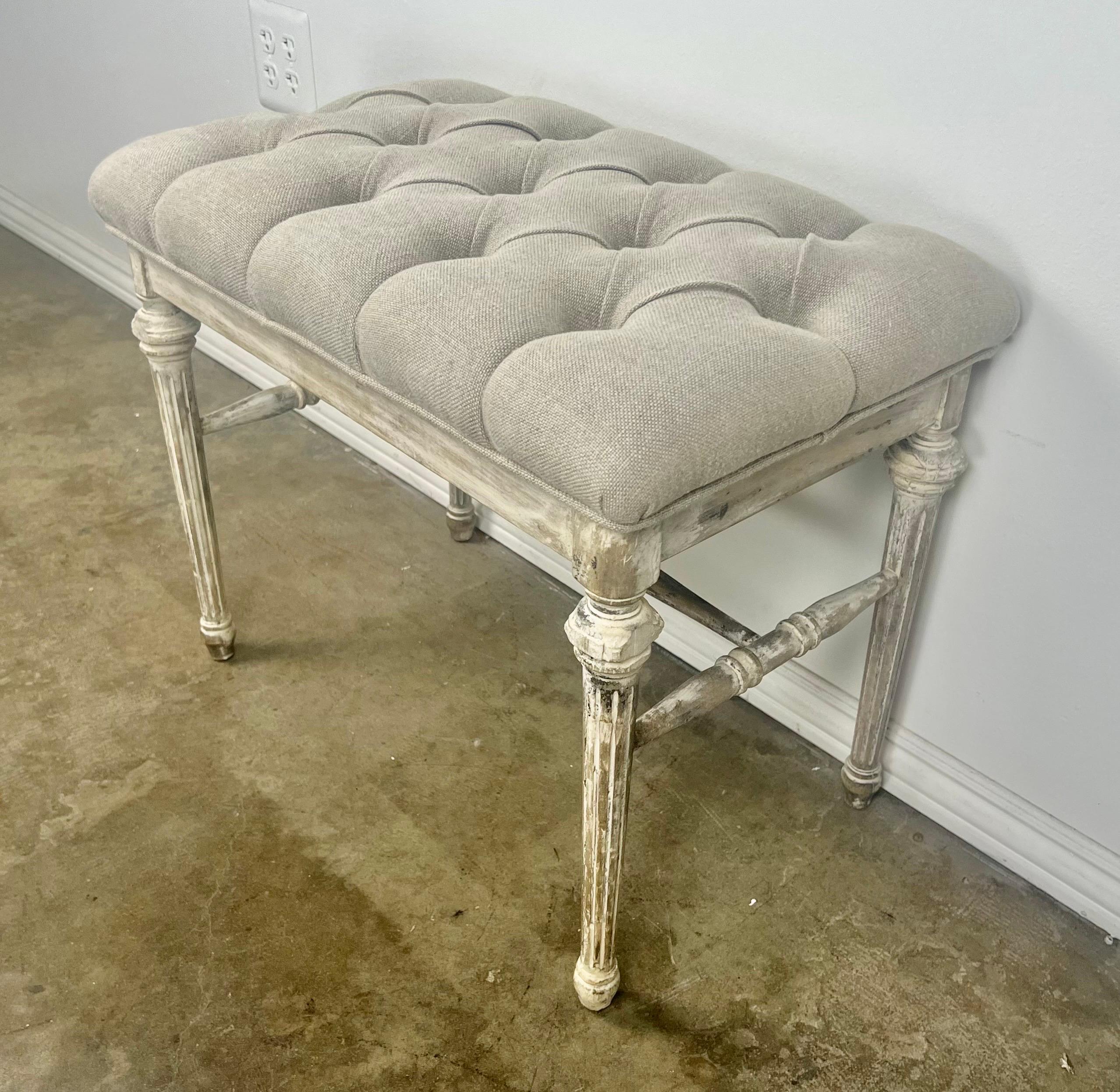 Charming French Louis XVI painted bench.  The bench stands on four straight fluted legs.  The paint is worn and only remnants remain.  Newly reupholstered in Belgium linen with nailhead trim detail.
