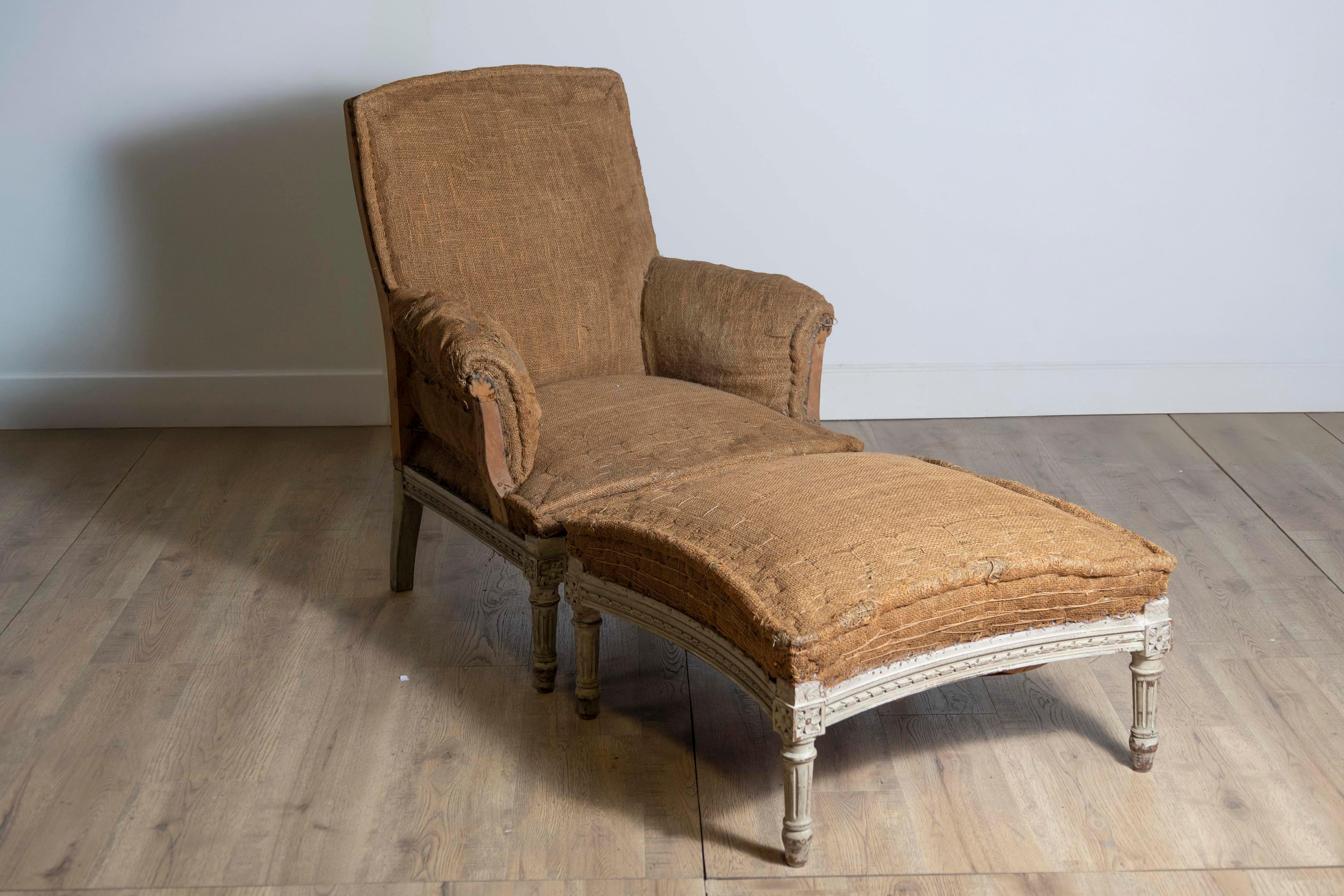 A French Louis XVI style painted wood bergère chair with matching ottoman circa 1870 with carved twisted ribbon motifs and fluted legs. Immerse yourself in the elegance of 19th-century French design with this Louis XVI style bergère chair and