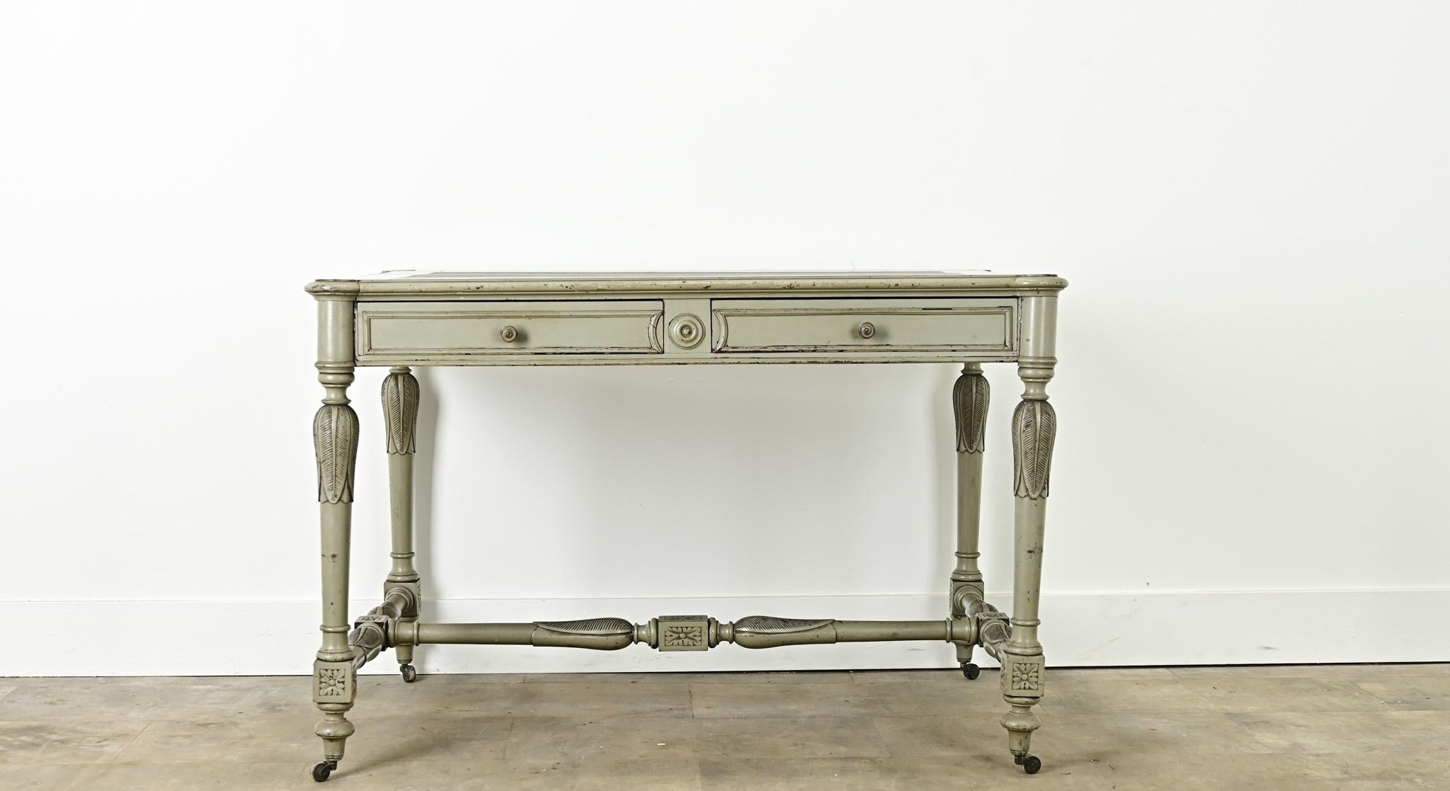A unique Louis XVI style painted desk made in France. This painted desk has a carved wooden frame with pronounced rounded corners and a worn inset faux-leather top. Below the writing surface are two paneled drawers with turned knobs. The desk legs