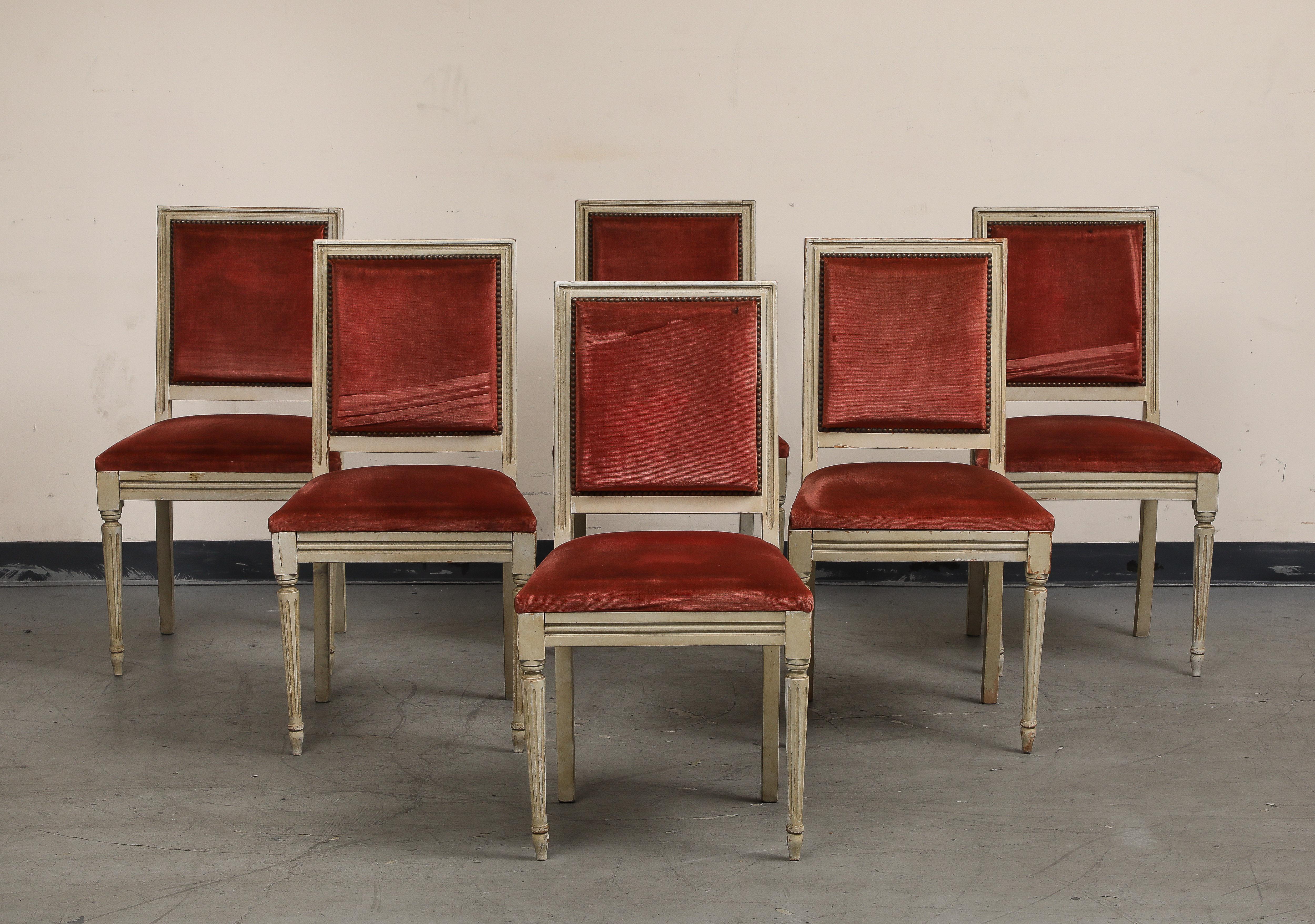 Set of six (6) early 20th century French Louis XVI style painted side chairs. Original paint/distressed finish on frames with fluted and tapered legs. Seat and back in red ribbed velvet upholstery and bronze nail head trim. 

