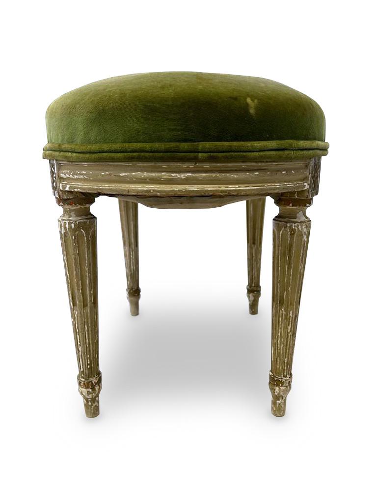 French Louis XVI Style painted stool with olive velvet upholstery with leaf and ribbon carved skirts on fluted legs. Perfect for a vanity or to place in a corner of a room. French-made this stool dates to the 1950s era. 

Property from esteemed