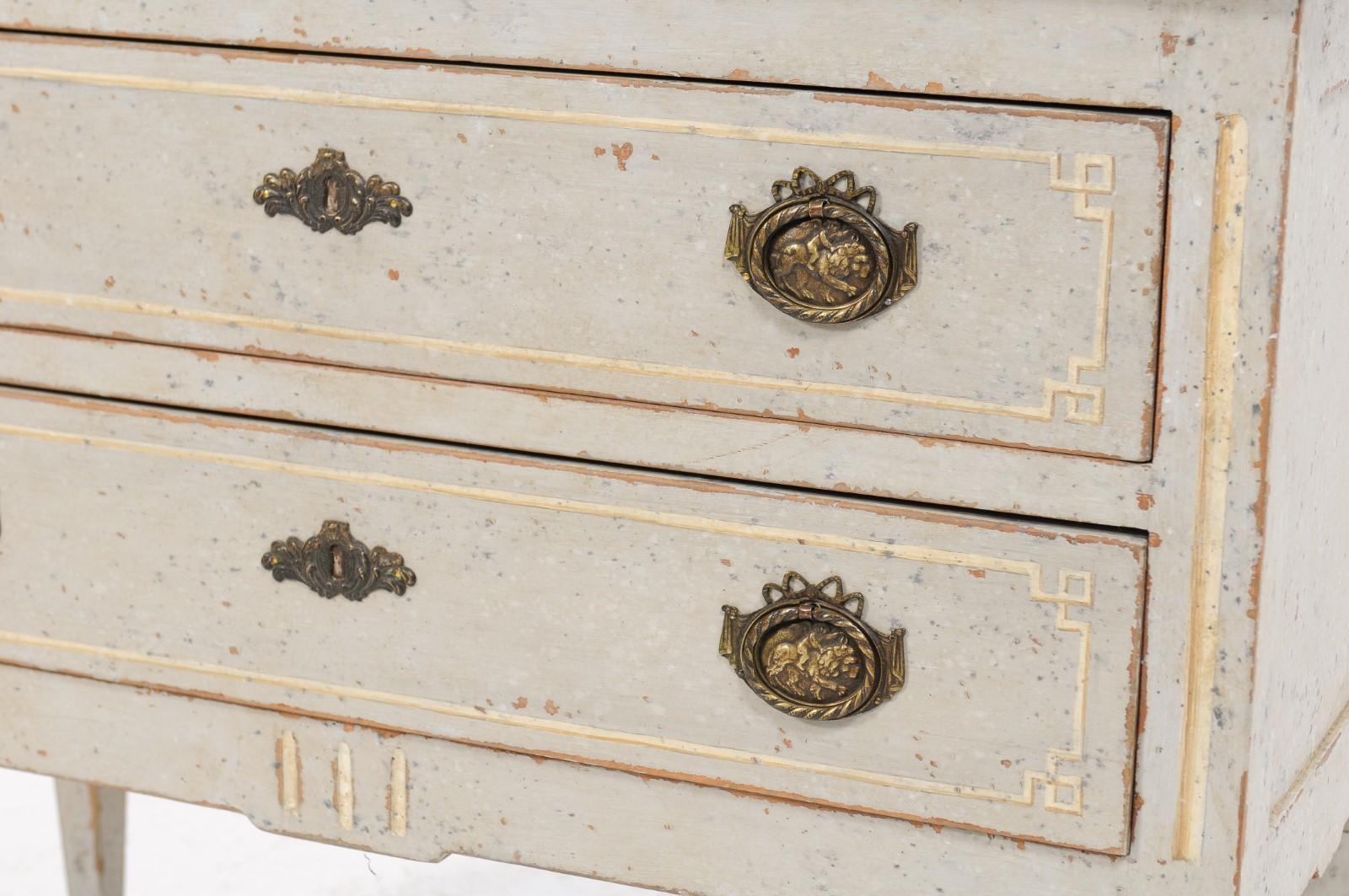 A French Louis XVI style painted two-drawer commode from the late 19th century, with black top, gilded accents and fluted, tapering legs. We spotted this pretty commode from afar and were awed by its pretty lines. With its fluted tapering legs,