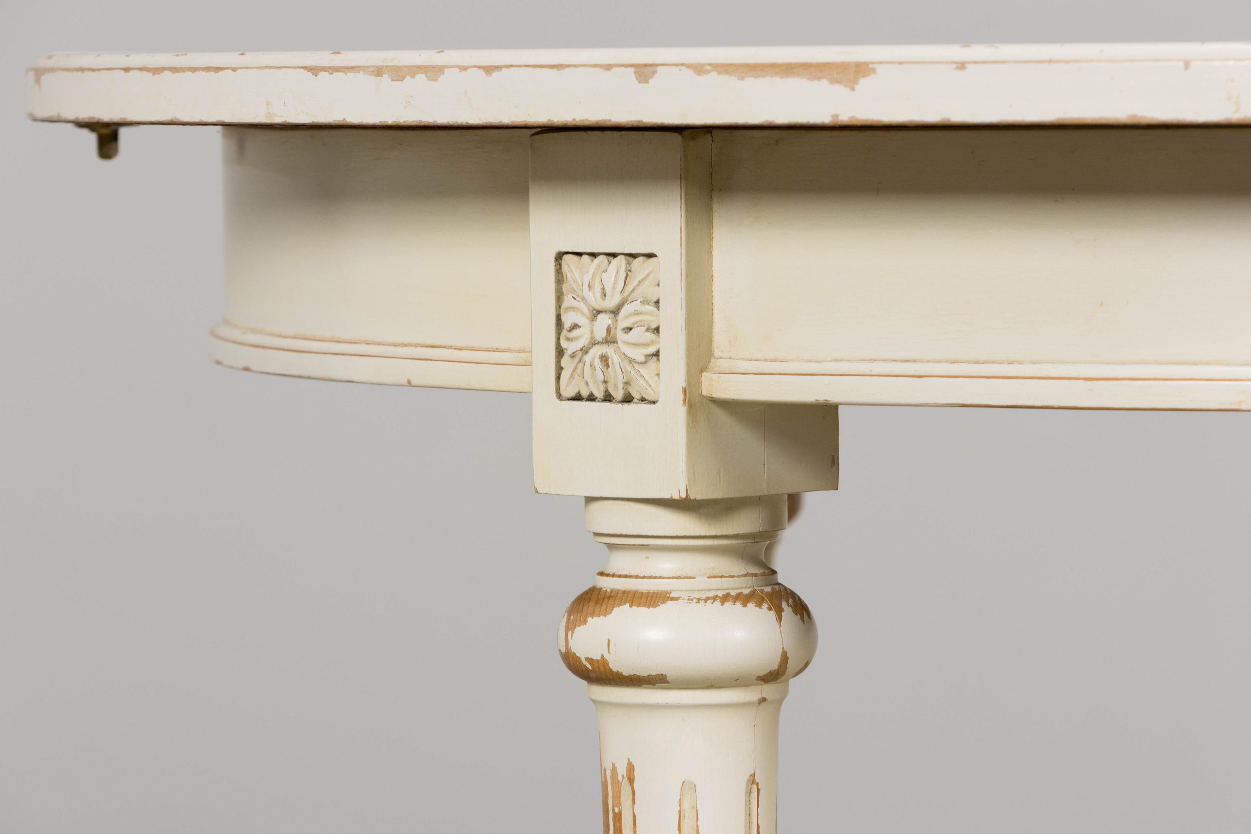 An elegant mid-20th century French Louis XVI style dining table, sourced in Provence. The table rests on four tapered, fluted legs capped with carved rosettes at the apron corners, all in a painted cream finish with distressed wear that evokes the