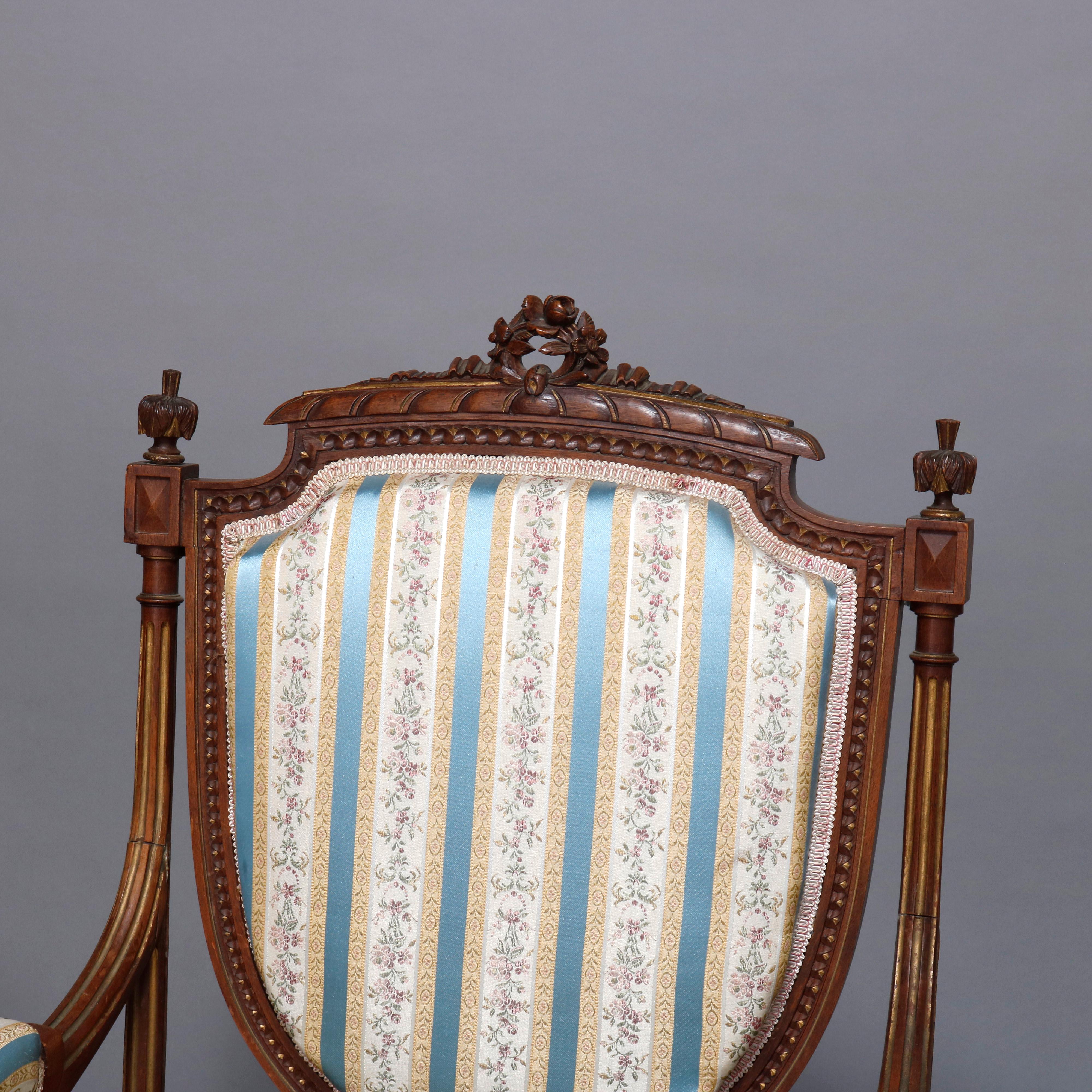 An antique French Louis XVI parlor set includes two armchairs and one side chair, each offers parcel gilt carved walnut frame with crest having pierced central wreath with flanking finials over upholstered back, arms and seat raised on fluted