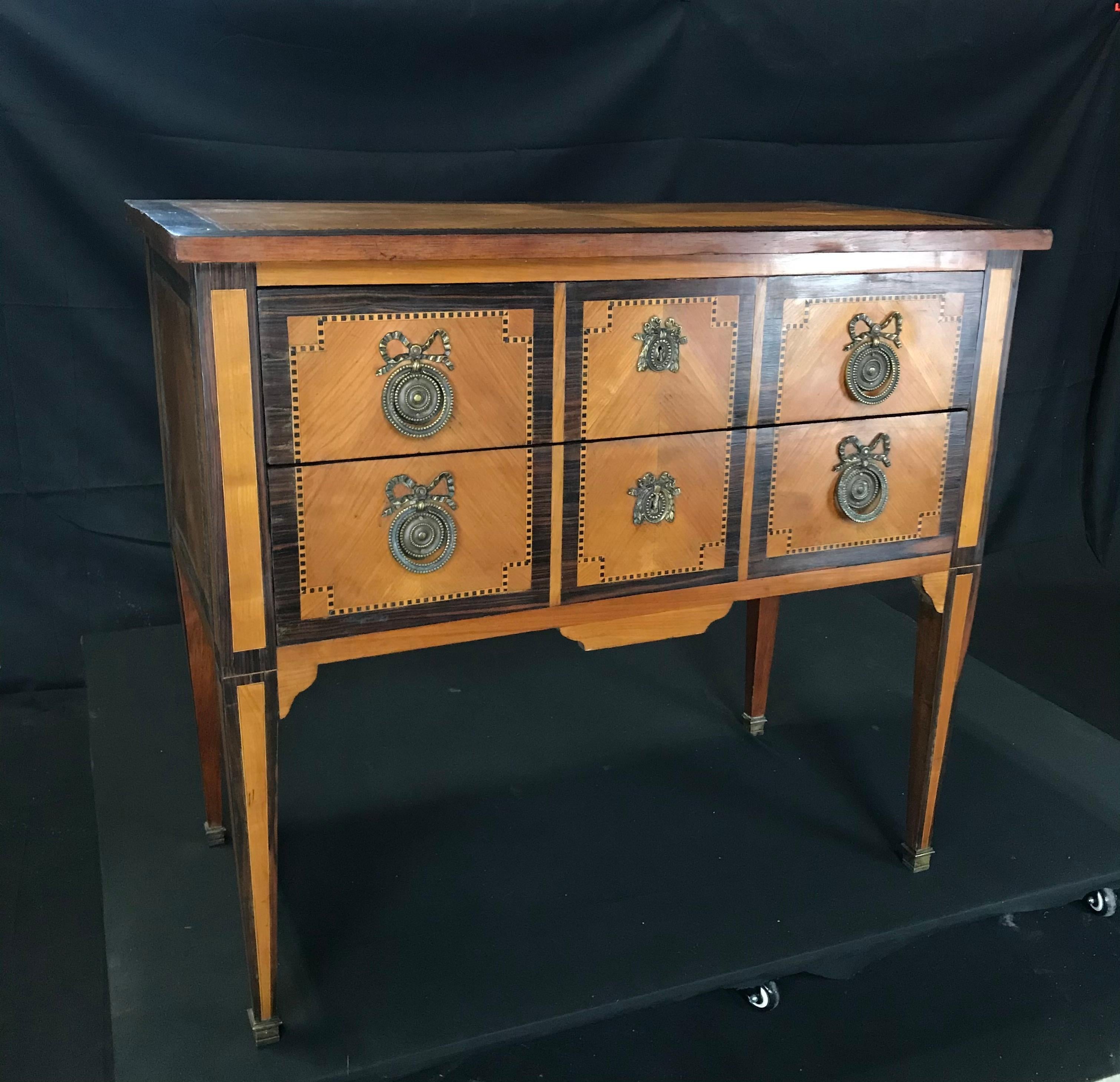 An exquisite inlaid petite commode on stand having an intricate marquetry top and body above two locking drawers with geometric inlay and bronze pulls and escutcheons on tapered legs ending in bronze ferrules. 

#5811




