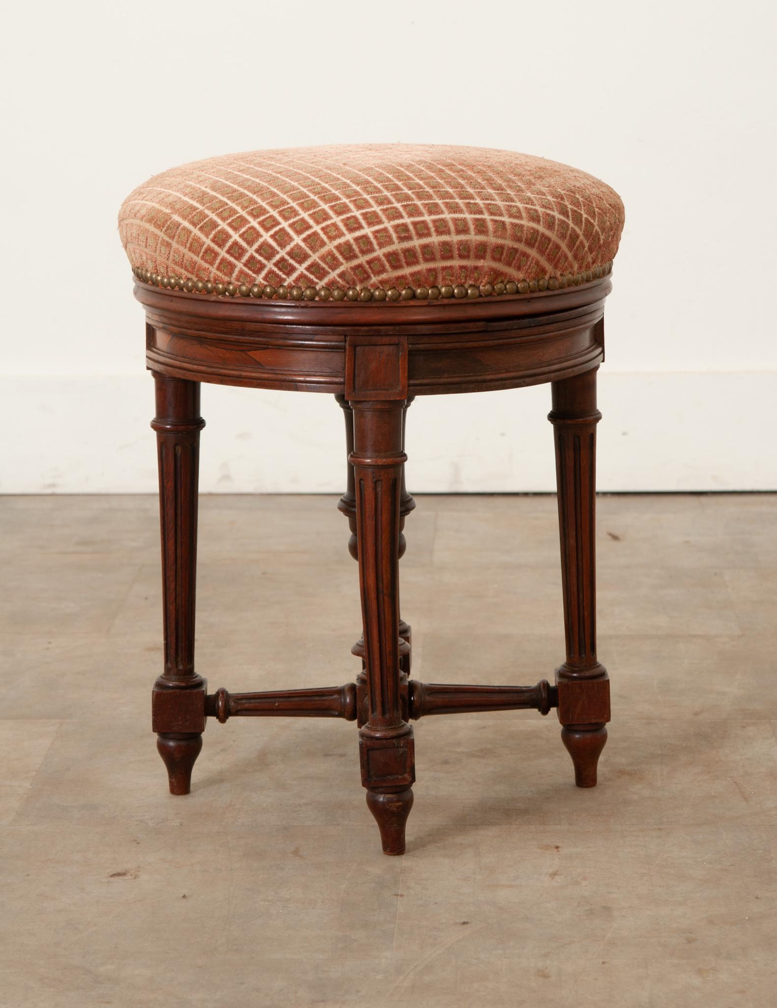 A round French piano stool made of carved rosewood and mahogany in the Louis XVI Style. The top cushion is made of cut velvet upholstery with nailhead trim. The center of the stool has a functioning steel screw to raise and lower the seat height