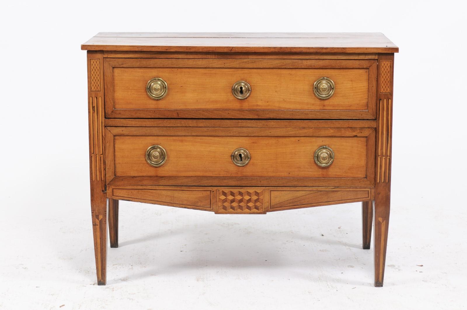 A French Louis XVI style pine and walnut two-drawer commode from the late 19th century with marquetry motifs, fluted side posts and original hardware. Born in Lyon during the last quarter of the 19th century, this beautifully proportioned Louis XVI