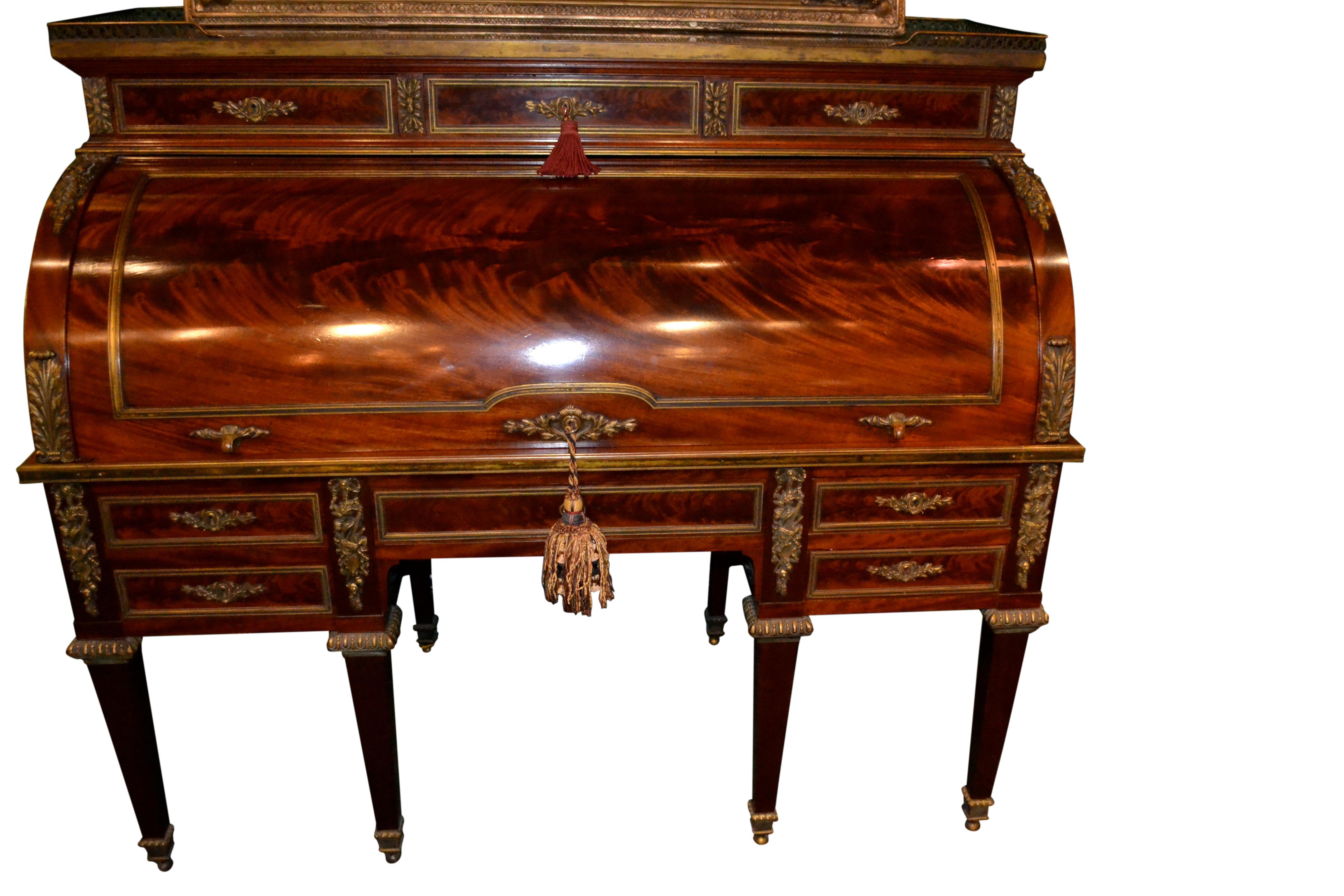 An imposing Louis XVI style roll top desk in beautifully figured mahogany and having finely chased and gilded bronze mounts; the green marble top with a bronze gallery above three long drawers, the open roll top reveals a number fitted drawers above