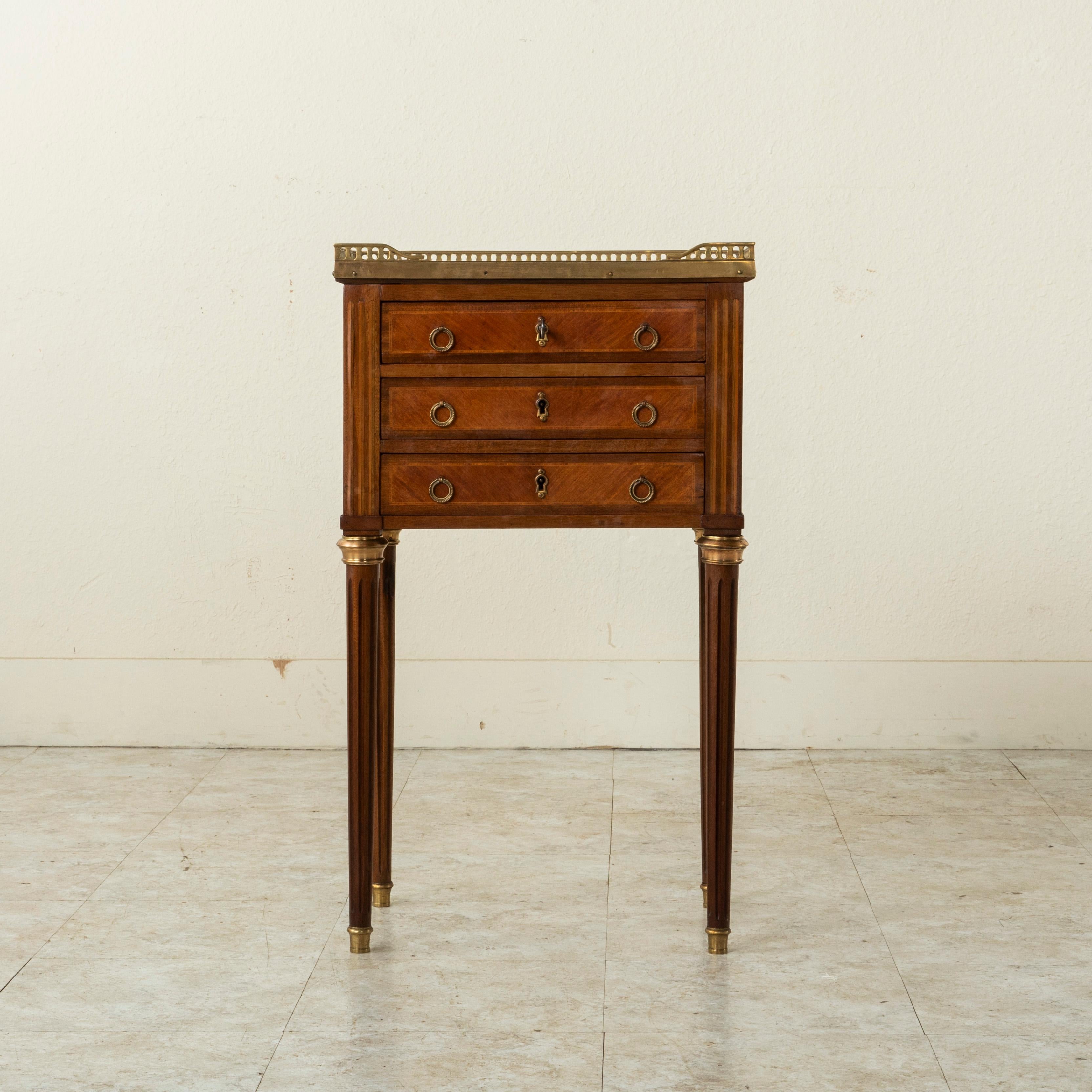 This early twentieth century French Louis XVI style rosewood side table or nightstand features inlaid fluted corners of sycamore and lemonwood. A pieced bronze gallery surrounds its white marble top. Its three drawers of dovetail construction are