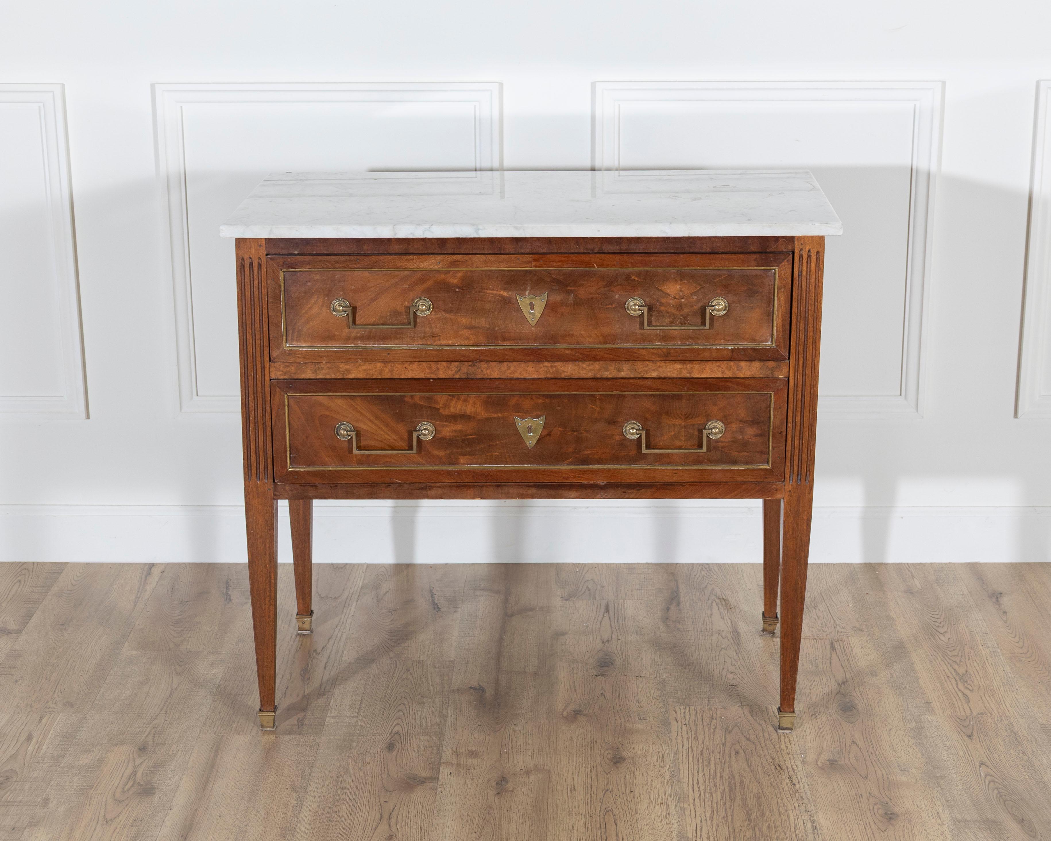 Cette élégante commode sauteuse de style Louis XVI a été fabriquée en France vers 1920 et présente des détails néoclassiques raffinés, tant au niveau de la structure que de l'ornementation. Construite en noyer massif et en placage de noyer, la
