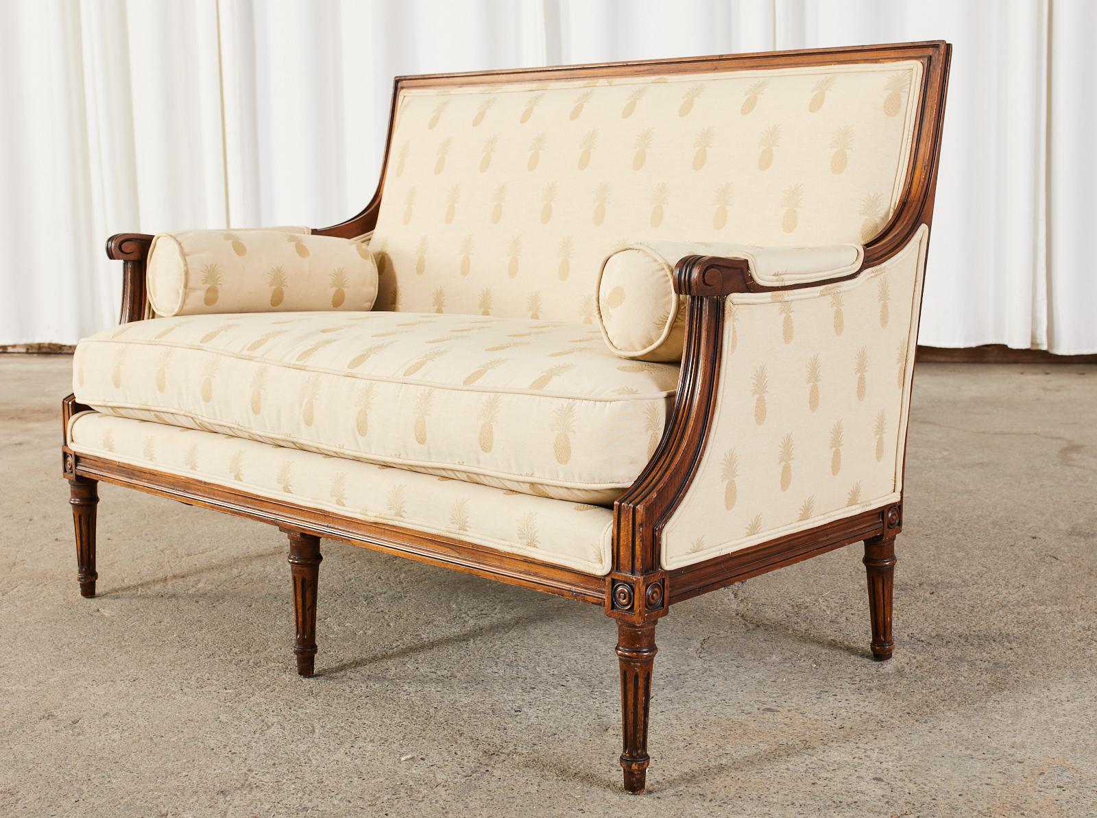 Handsome French Louis XVI style settee canape with a beautifully carved frame. The settee features a Tommy Bahama style cream colored upholstery with a Caribbean pineapple motif. The square back, molded frame has gracefully curved padded arms