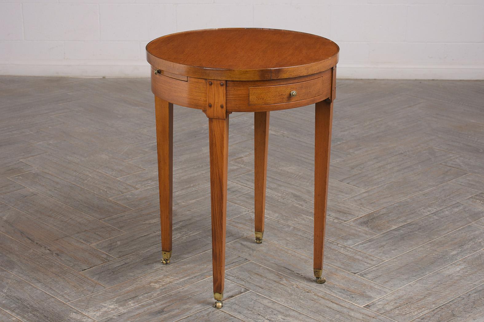 This French late 19th century Louis XVI style side table is made out of cherrywood stained a light walnut color. It features a wooden top, two small drawers with brass knobs, and 2 pull leaves with gilt embossed leather inserts. It rests on four