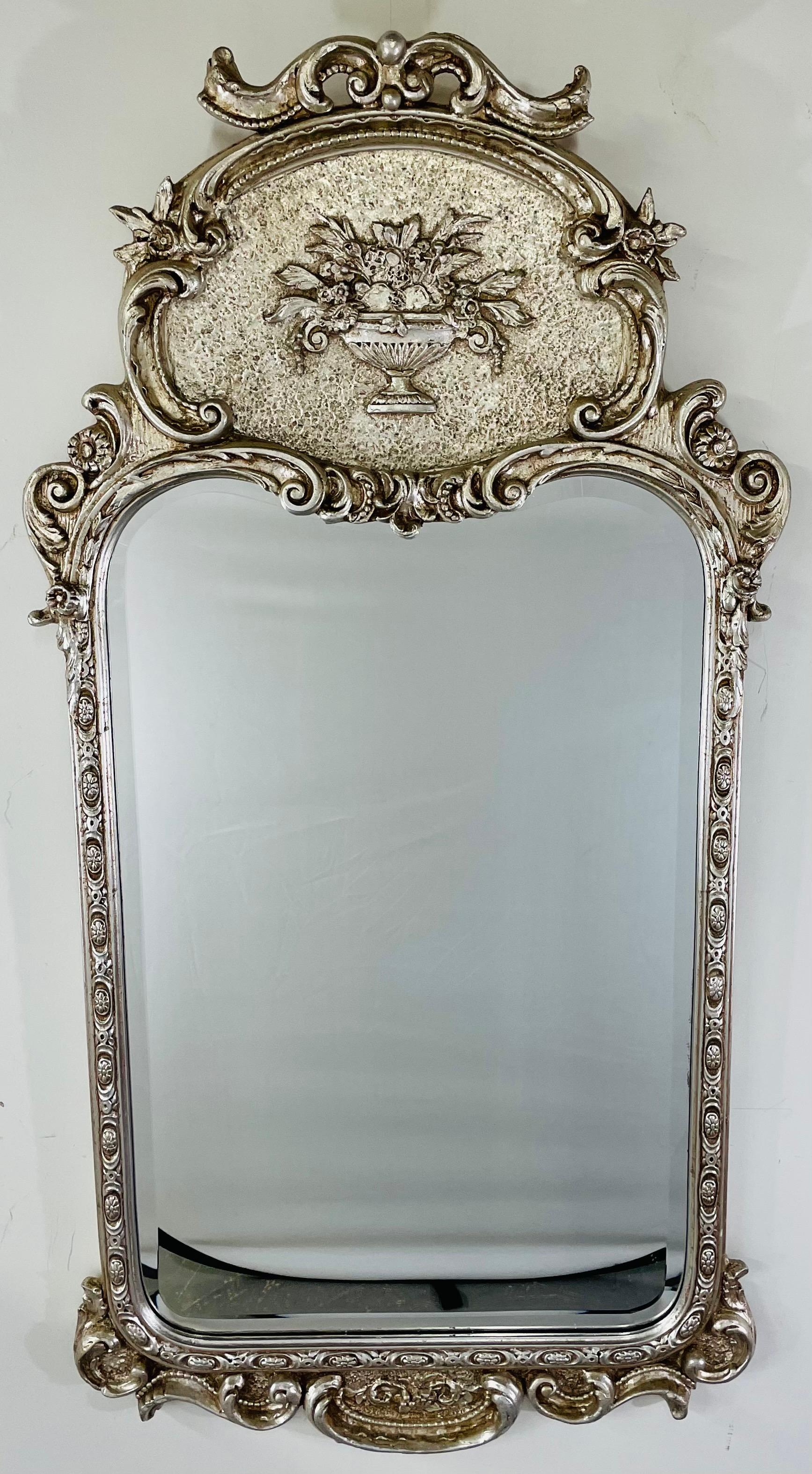 An early 20 century French Louis XVI Trudeau mirror. The beautiful mirror features fine carving and design. The top panel presents a vase with flowers and the frame shows acanthus floral and scroll motifs. Painted in a silver gray, the mirror boasts