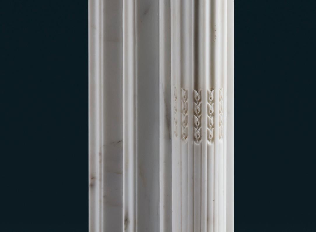 Eine antike französische Kaminumrandung im Louis-XVI-Stil aus bestem weißem Marmor, das geformte Regal über dem Fries mit reliefartig geschnitzten Lorbeerzweigen, die Pfosten mit Akanthuskapitellen auf dreiviertelgeteilten, kannelierten Säulen, die