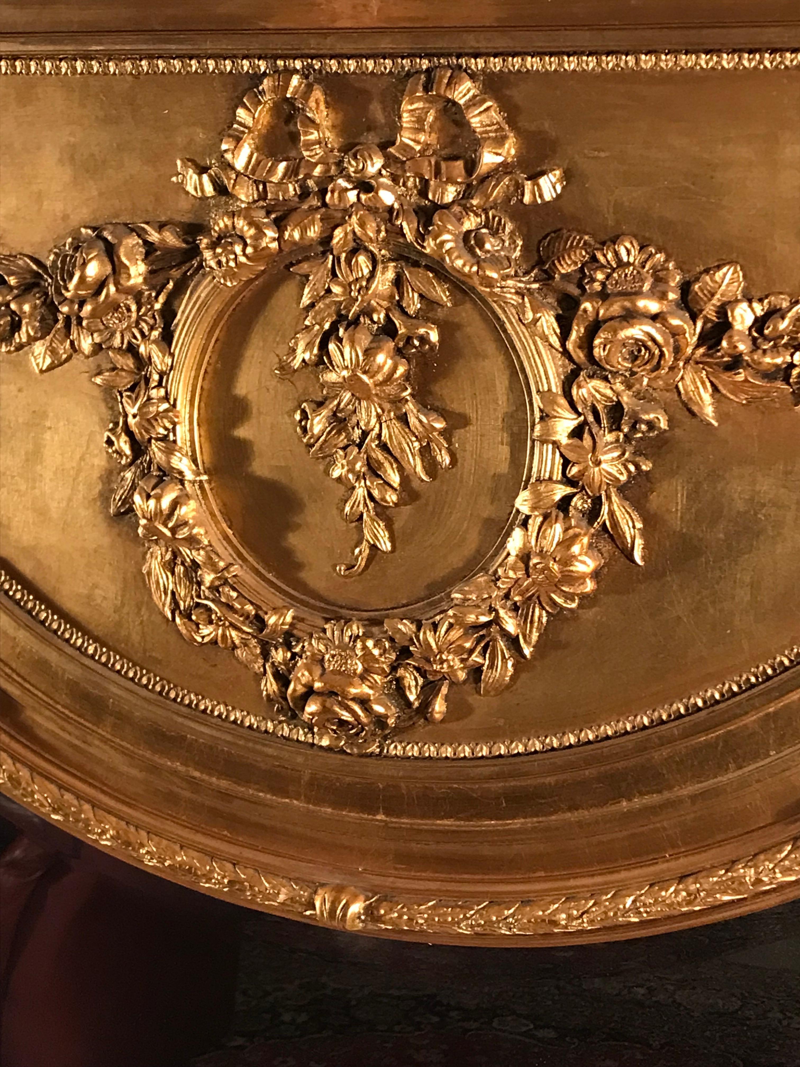 Cet impressionnant miroir à trumeau de style Louis XVI se distingue par sa belle décoration de fleurs et de feuilles. La partie supérieure présente une magnifique guirlande de fleurs/roses avec un médaillon central. Le miroir en bois doré est en