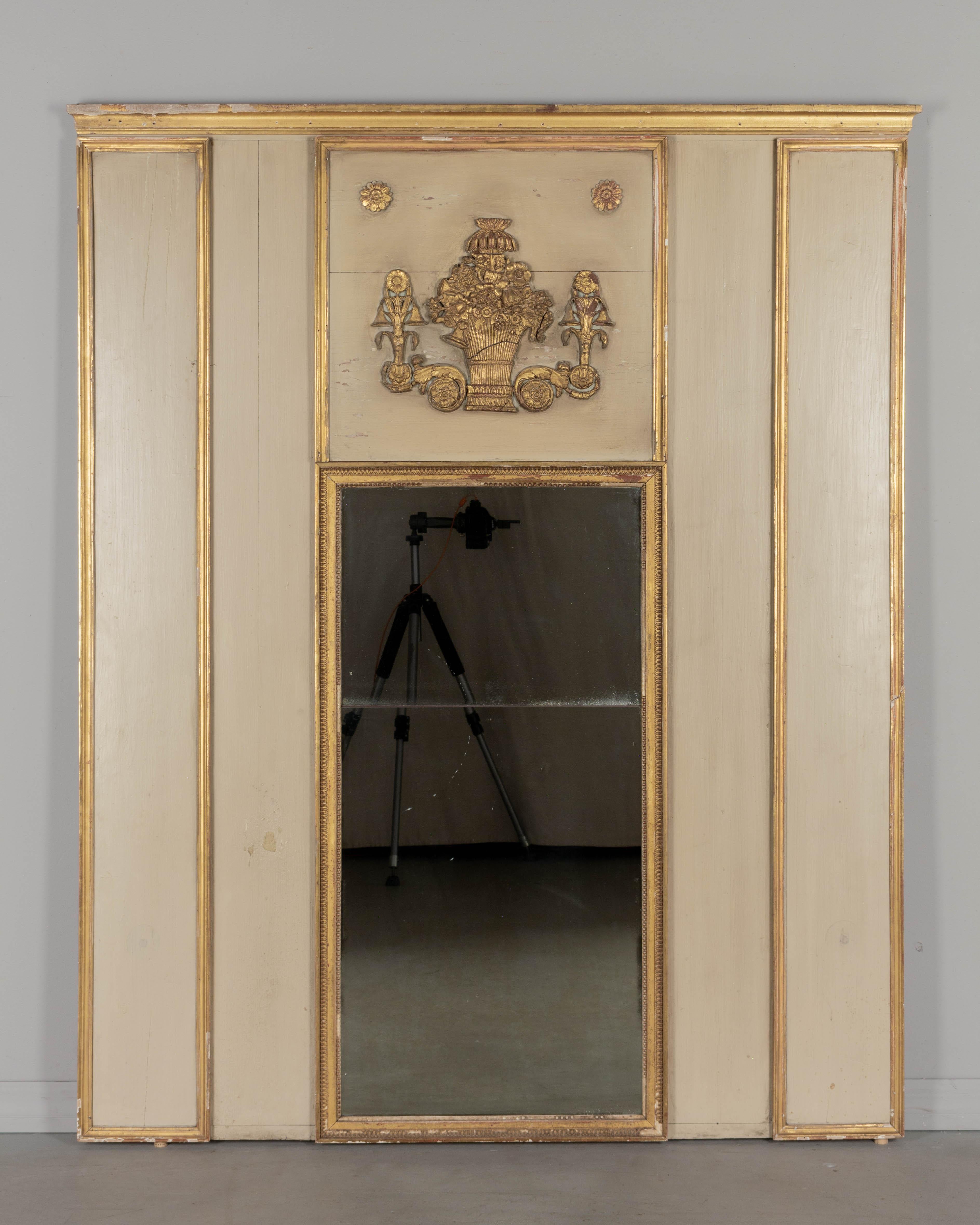 Specchio trumeau francese in stile Luigi XVI dell'inizio del XX secolo con cornice in pino dipinto e finiture dorate. Applicazione in rilievo in legno dorato intagliato di un grande cesto di fiori, volute e rosette. Magari da una veranda o da un