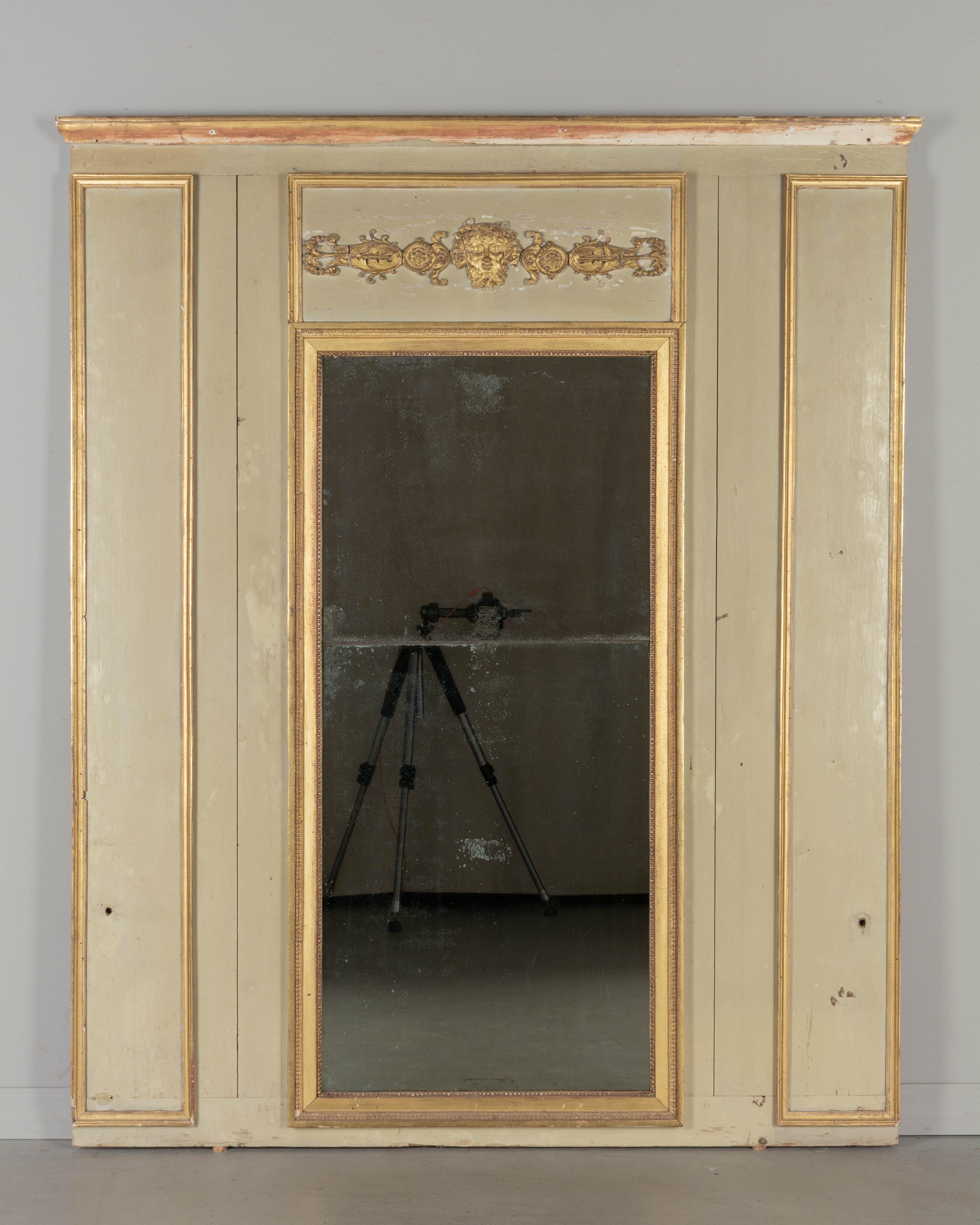 Specchio trumeau francese in stile Luigi XVI dell'inizio del XX secolo con cornice in pino dipinto e finiture dorate. Applicazione decorativa in legno dorato intagliato con testa di Bacco, volute e rosette. Magari da una veranda o da un giardino