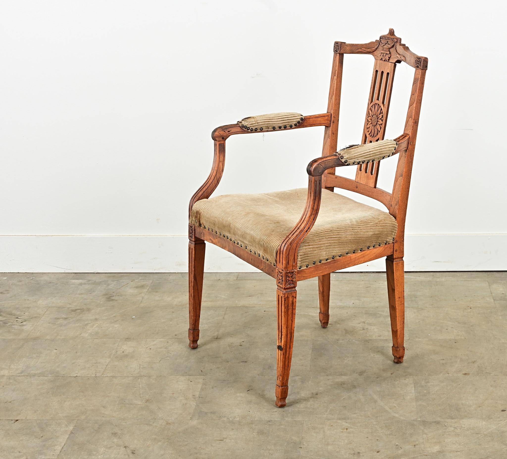 Una poltrona francese in stile Luigi XVI del 1800 o precedente. Questa robusta poltrona in legno massiccio di quercia è interamente intagliata a mano con un'urna in cima allo schienale della sedia con volute e un medaglione floreale centrale. I