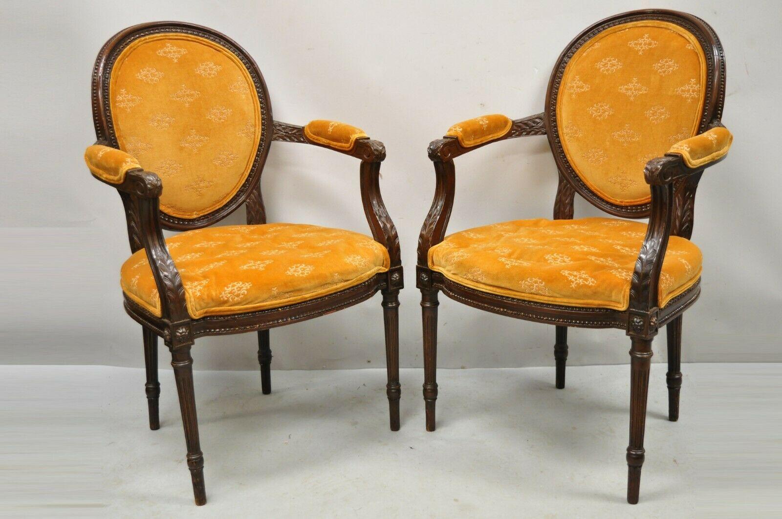 French Louis XVI Style Upholstered Oval Back Dining Arm Chairs - a Pair. Item features upholstered and carved oval backs, solid wood frames, upholstered armrests, nicely carved details, tapered legs, great style and form. Circa Mid 20th Century.