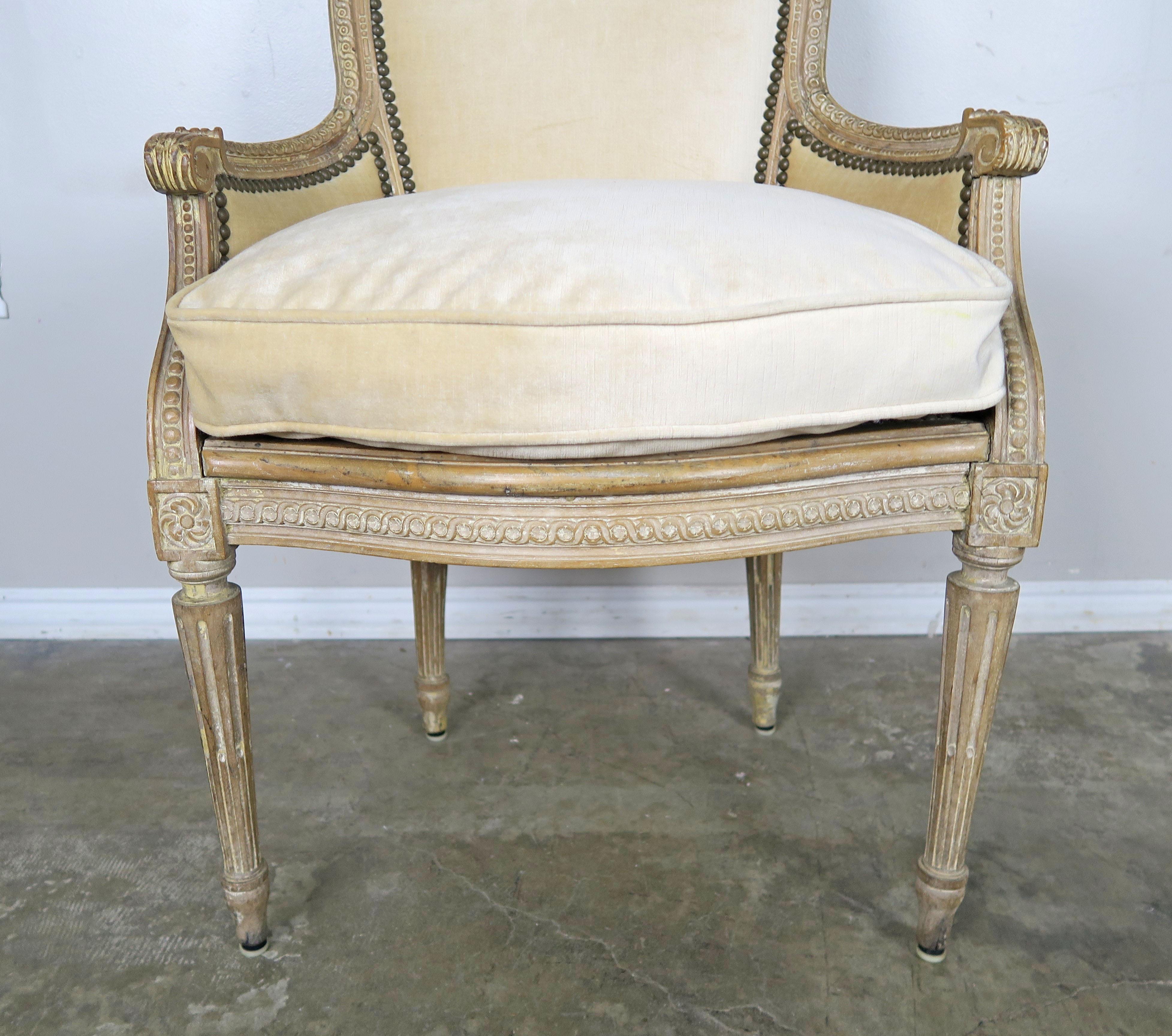 Charming French Louis XVI style carved occasional or vanity chair in a natural wood finish. The chair is newly upholstered in a cream colored velvet and finished with antique bronze colored nailhead detail. The frame is intricately carved with
