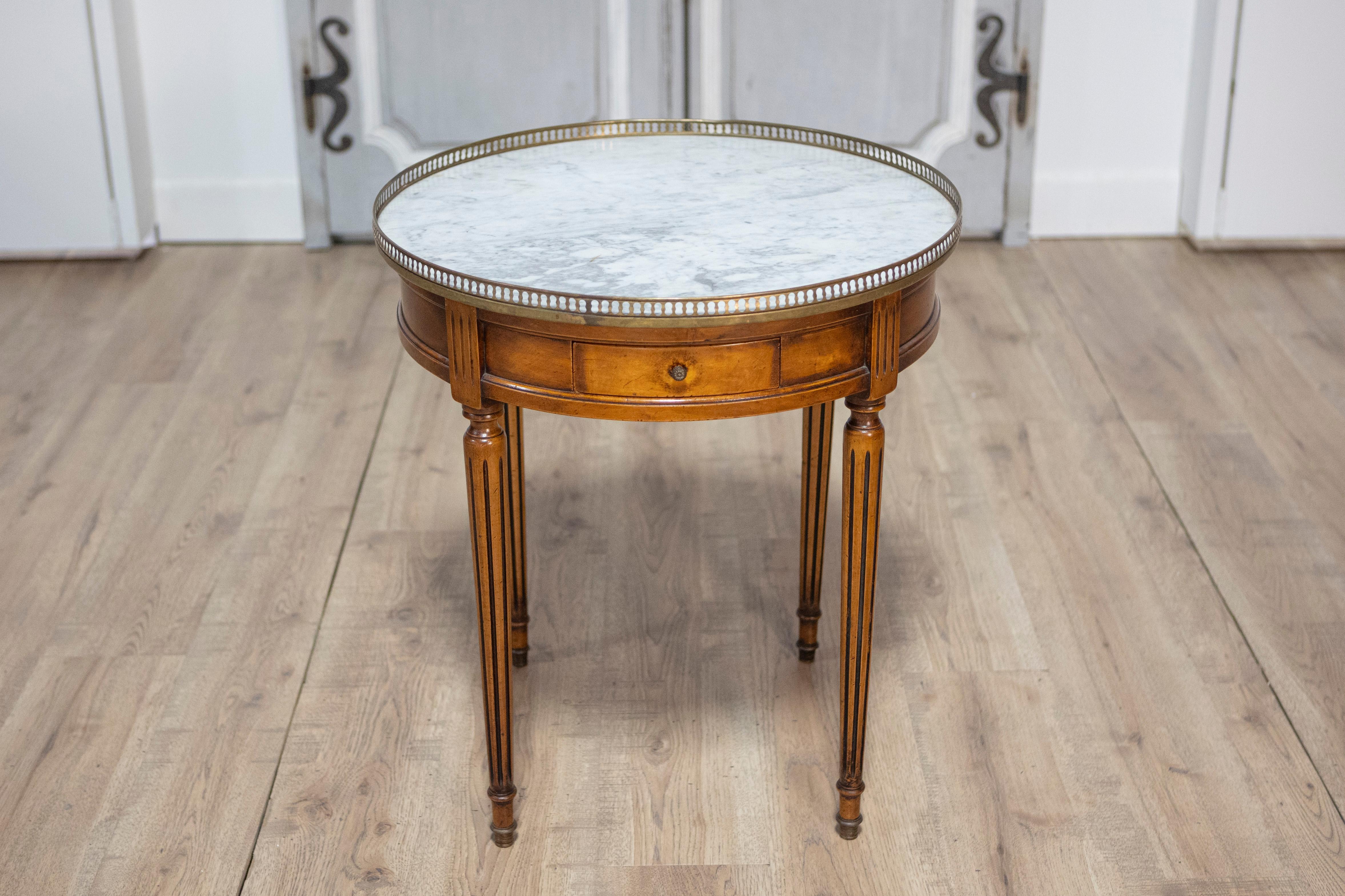 Mesa bouillotte francesa de nogal del siglo XX, estilo Luis XVI, con tablero de mármol abigarrado blanco y gris, galería de latón calado y patas acanaladas. Esta exquisita mesa bouillotte francesa de nogal estilo Luis XVI del siglo XX es una mezcla
