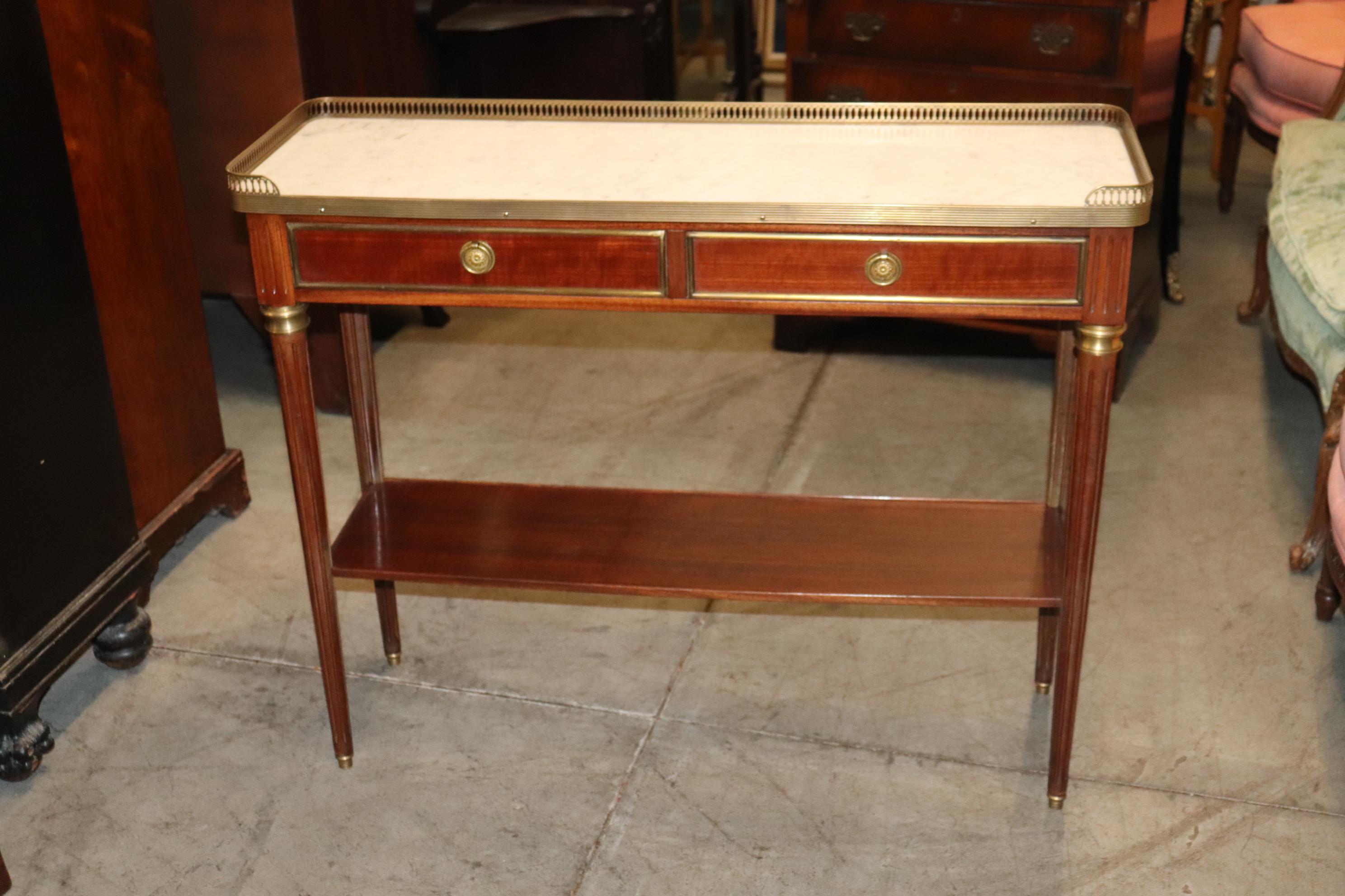This is a fantastic small and extremely narrow table with a finished back that can be used as a sofa table. The table is brass and bronze mounted and has a gorgeous slab of carrara marble inset on top with a brass gallery. The table measures 31 tall