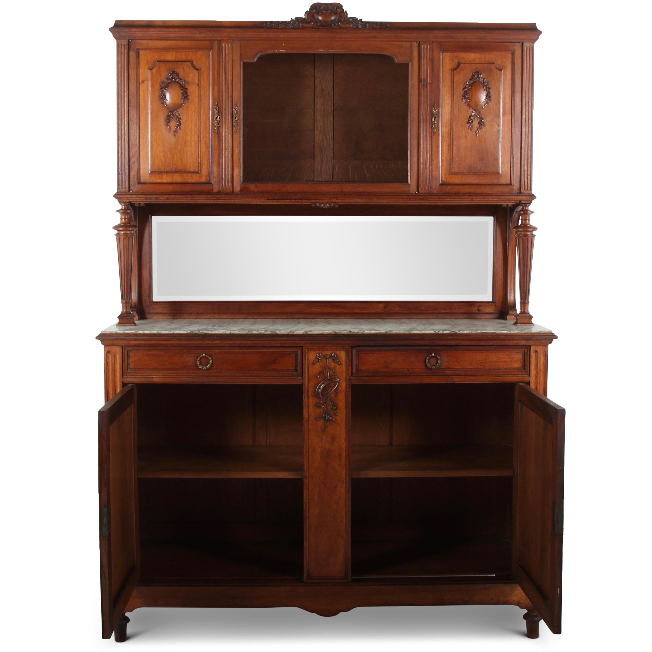 A French carved walnut Louis XVI style buffet Deux Corps, the top with a central glass door flanked by panelled and carved doors and raised on turned fluted columns. The marble-top base has two raised-panelled doors below two drawers and a central