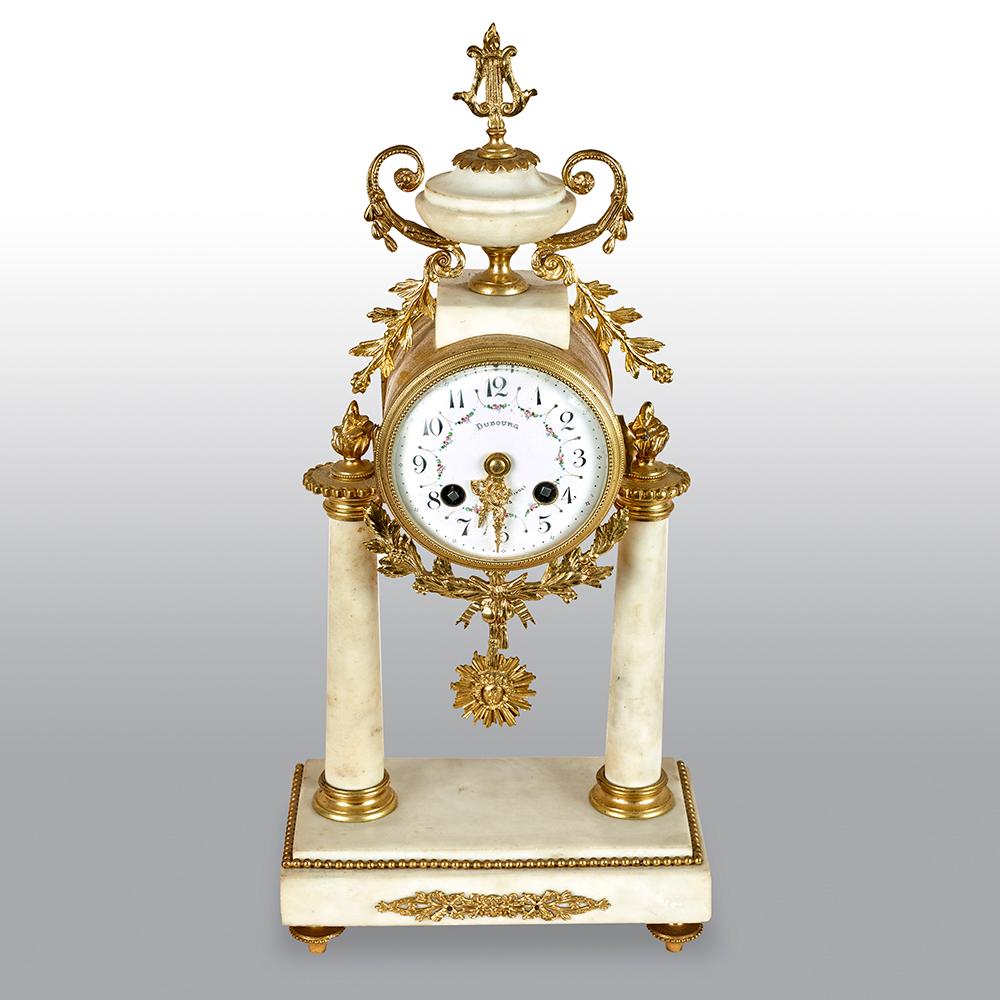 White marble and gilt metal mounted clock set, the clock surmounted with an urn above a four inch white enamel dial. The two train movement striking a bell, flanked by circular tapered columns raised on a shaped base together with two side pieces.
