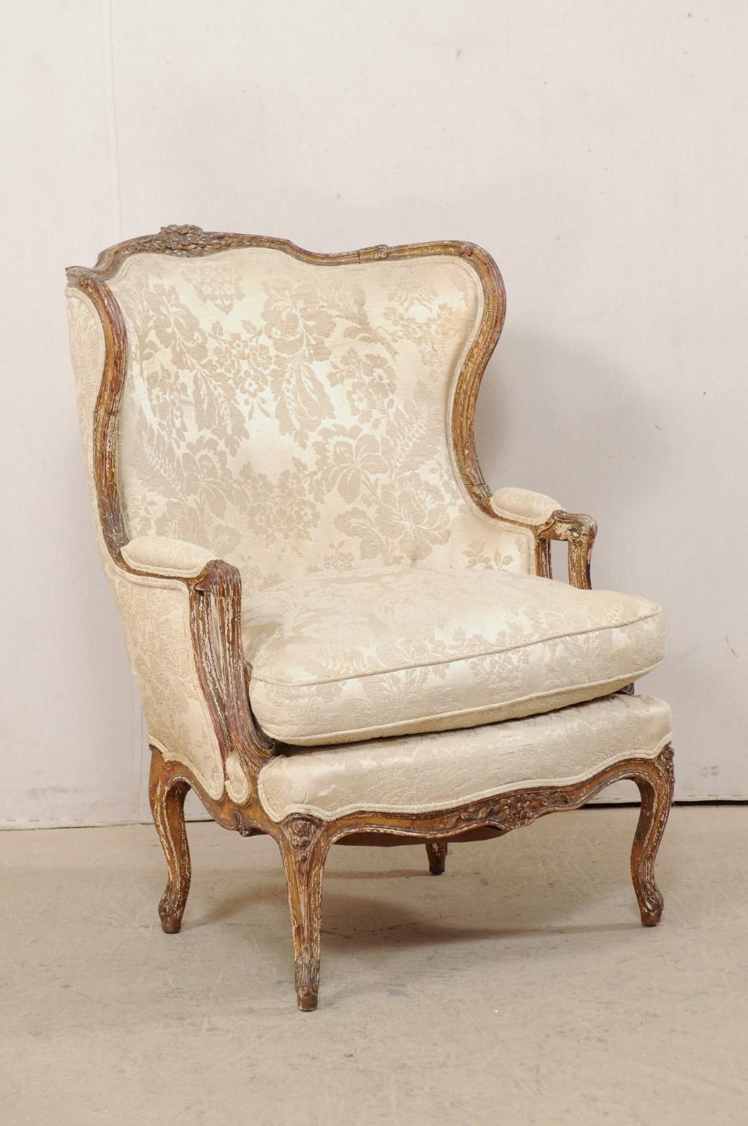 A French Louis XVI style winged back bergère chair, with it's original paint, from the 19th century. This antique chair from France features an elegant and shapely winged back, with finely carved wood trim about the crest and arms with a foliate