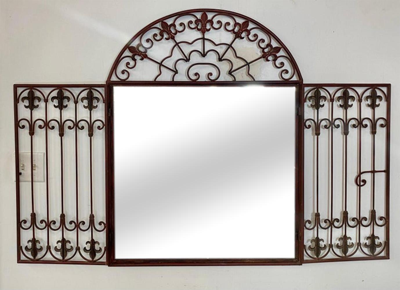 A charming French Louis XVI style wrought iron mirror in a Mediterranean design fashion. The wrought iron frame is finely crafted showing scrolls and fleur de lis motifs and having two doors opening to reveal the mirror inside.  The color of the