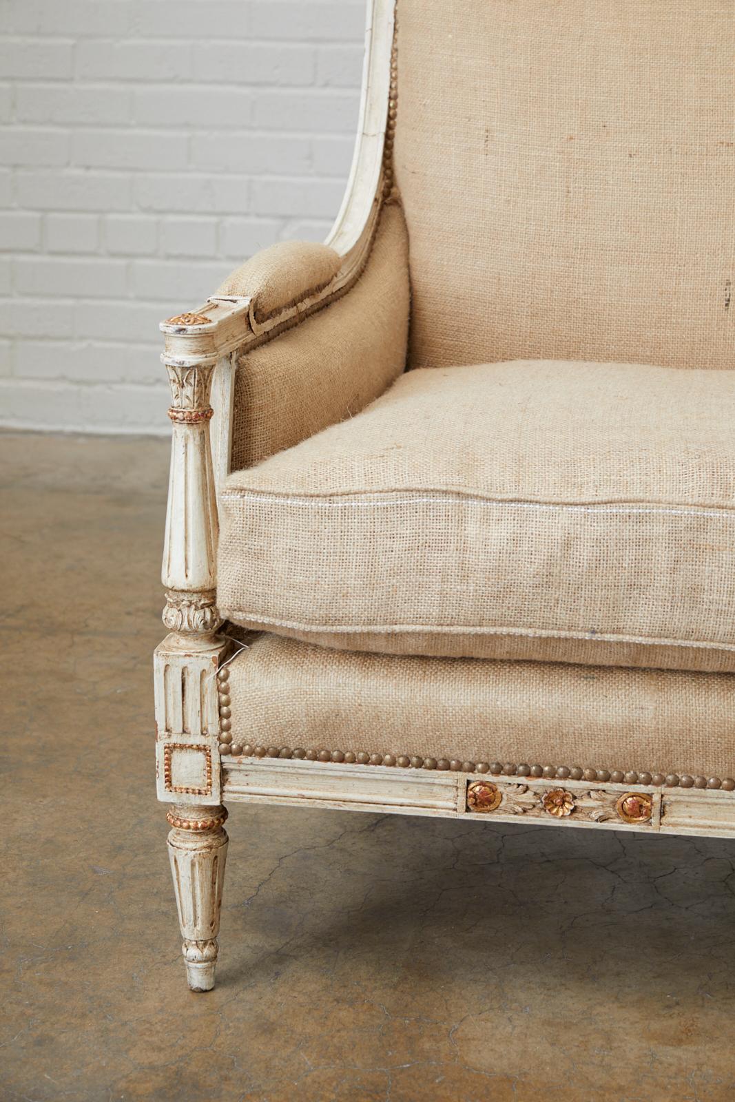 Stunning French painted settee or loveseat made in the Louis XVI Gustavian taste. Features a beautifully carved frame with neoclassical acanthus motifs. Each side has Directoire style column arm supports with a gilt rosette on the top. The flat