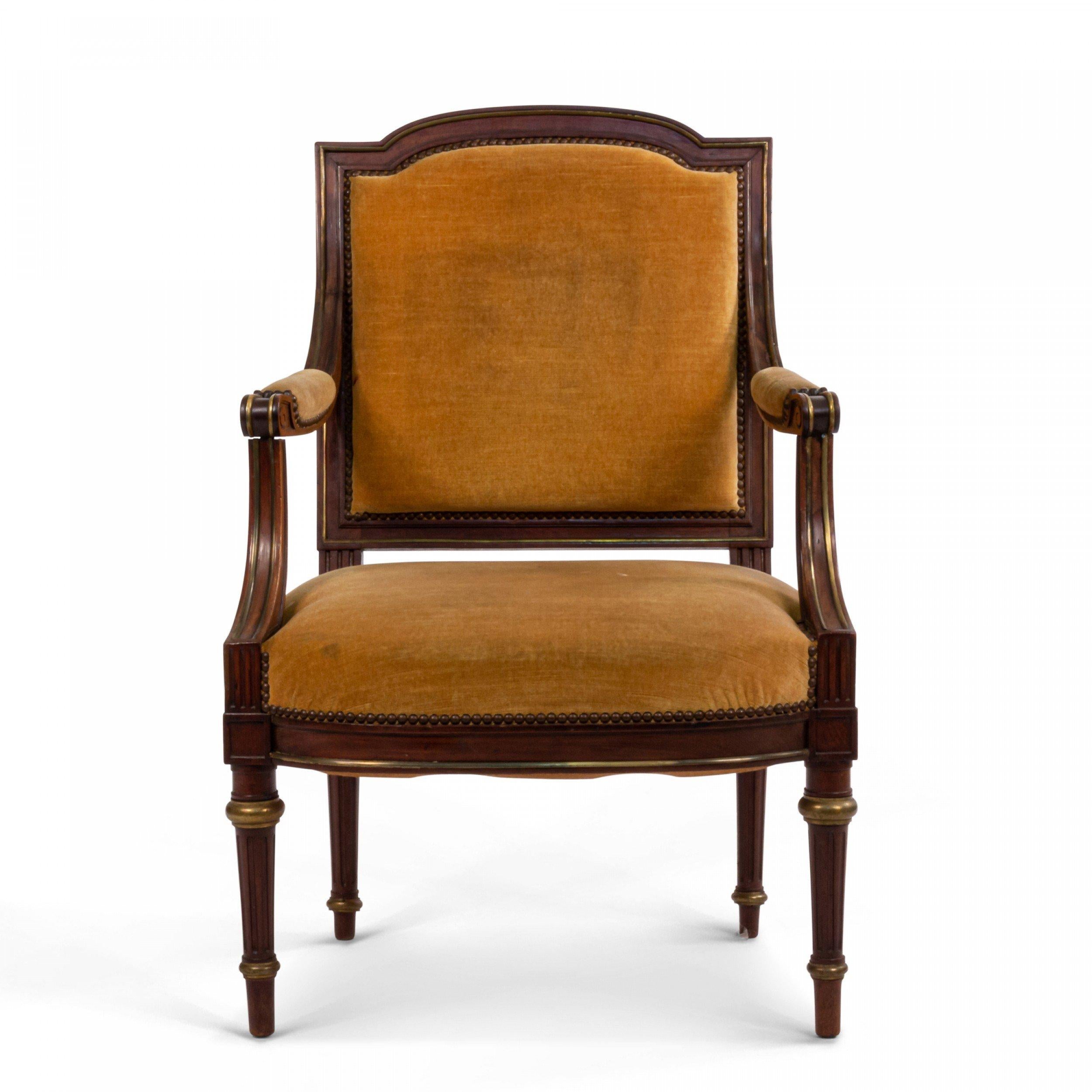 French Louis XVI style walnut arm chair with mustard yellow velvet upholstered back, seat, and armrests with brass trim detail.
       