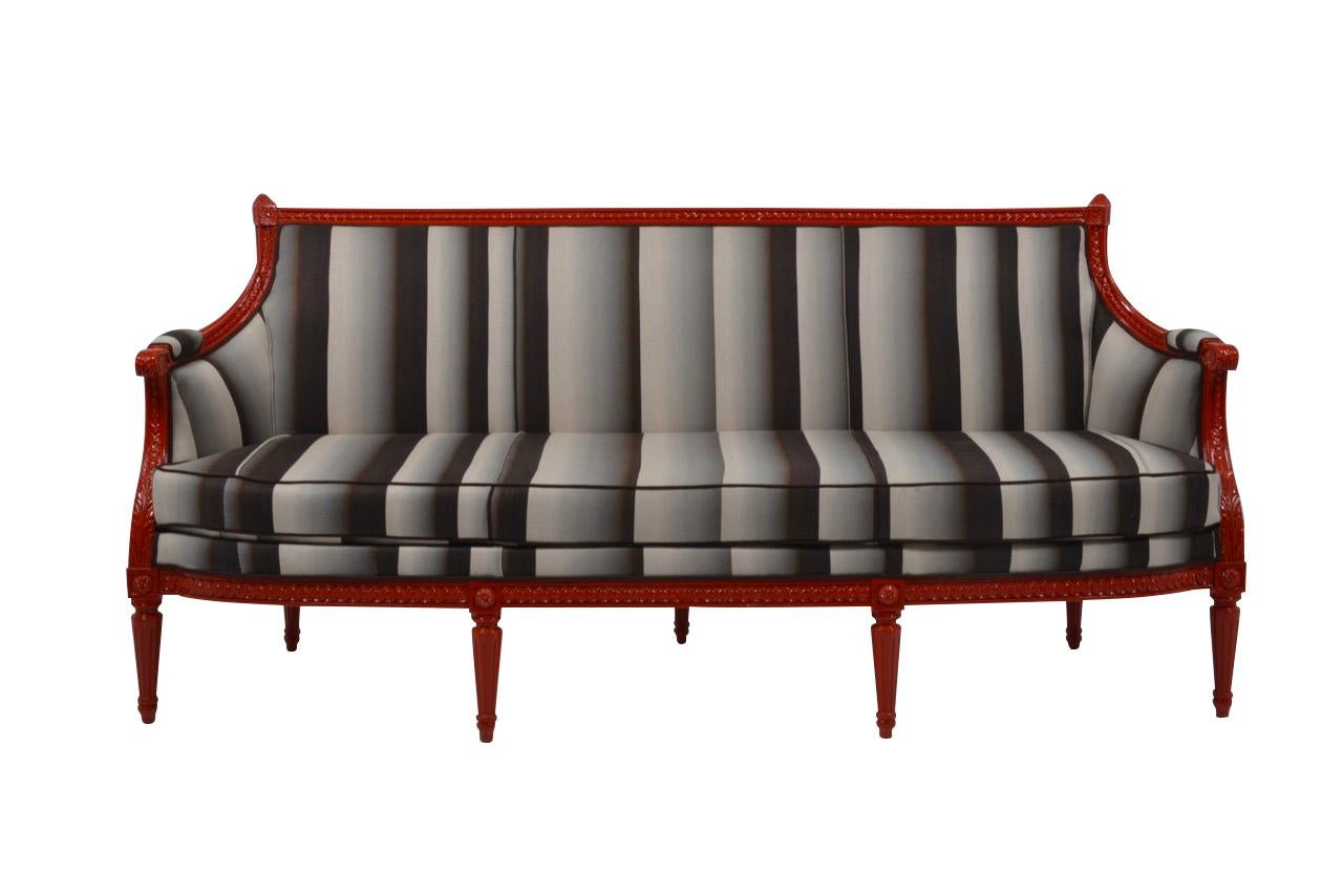Extremely elegant neoclassical settee called “en corbeille”, the arms wraparound the sides like a basket. Lacquered in a striking red and newly upholstered in a vertically grisaille colored and striped linen. Tapered and fluted legs. 3-seat.