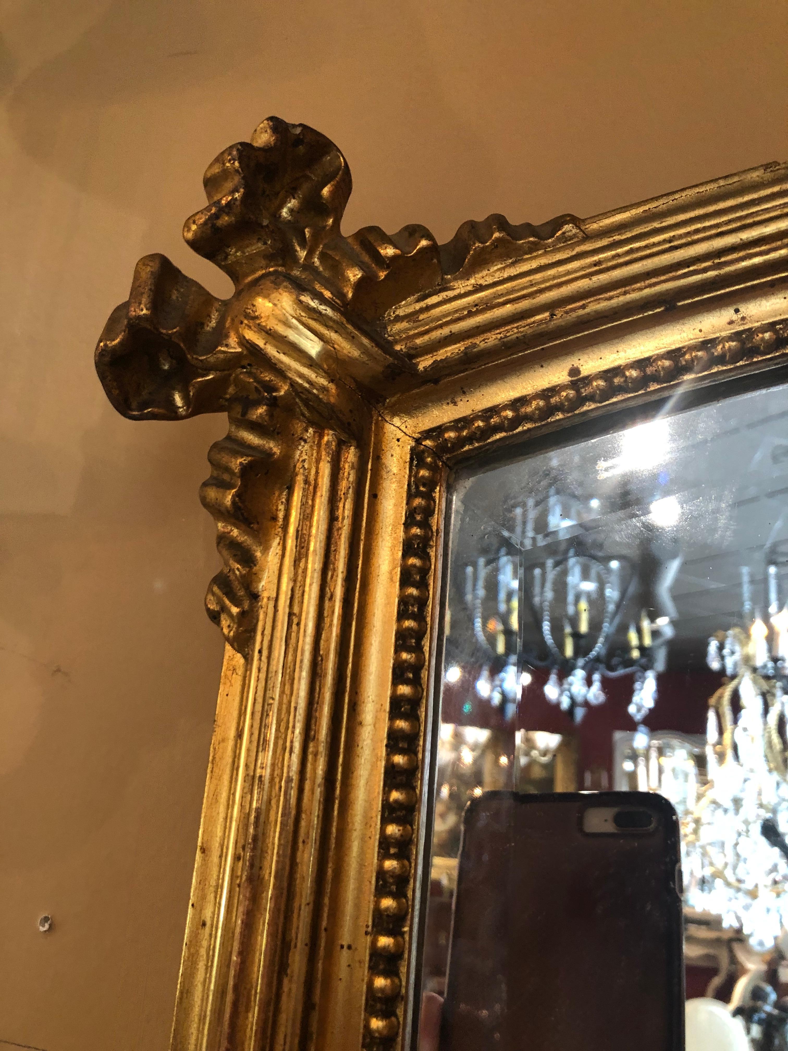 Miroir français de style Louis XVI en bois doré, 19ème siècle. Avec des motifs de rubans et de feuillages,
Garniture perlée, entourant la plaque de miroir biseauté.