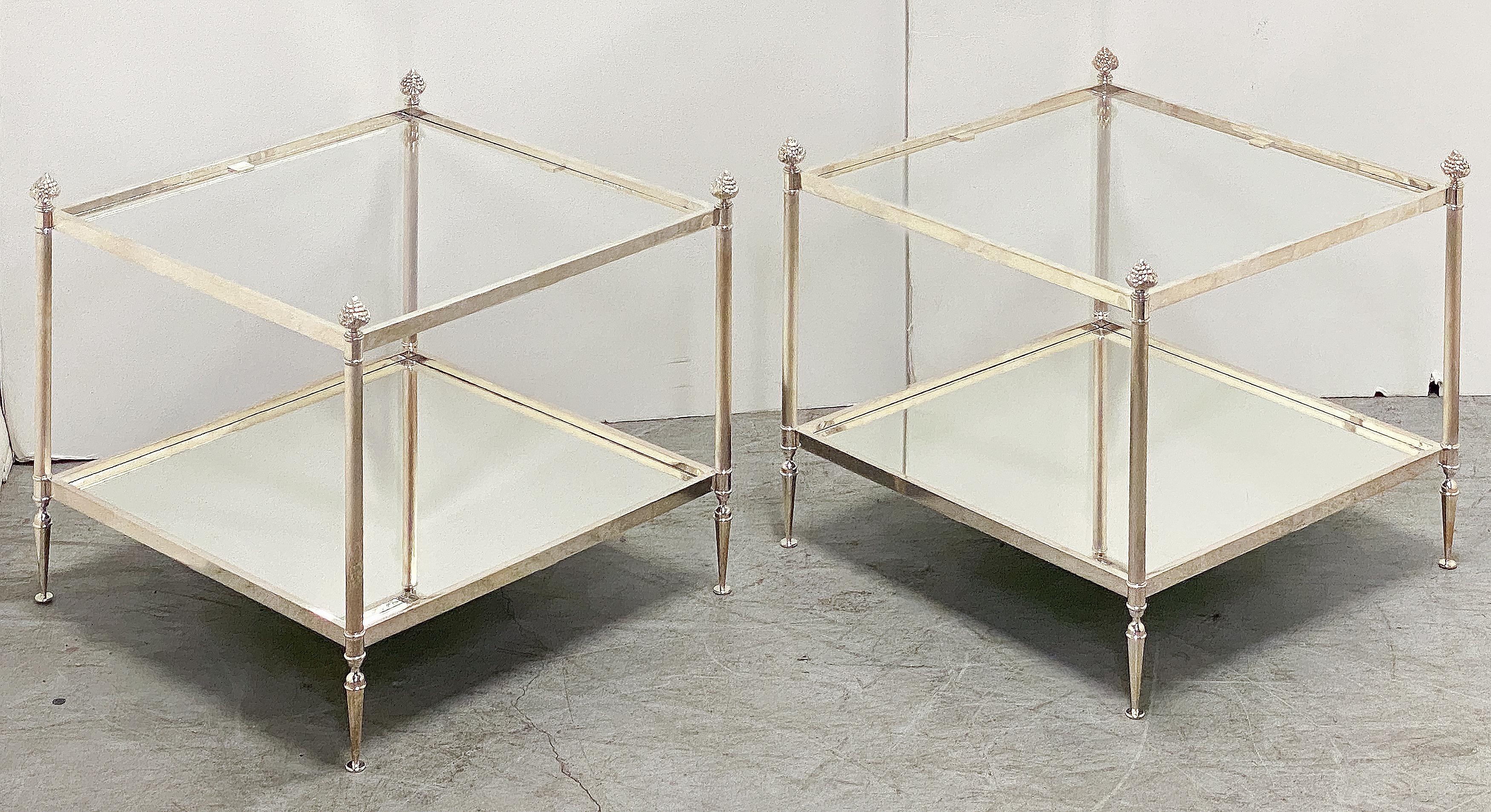 Una coppia di eleganti tavolini bassi francesi a due livelli in stile Mid-Century Modern - ogni tavolino presenta un piano quadrato in vetro inserito in una struttura metallica argentata e un piano inferiore con un pannello in vetro a specchio -