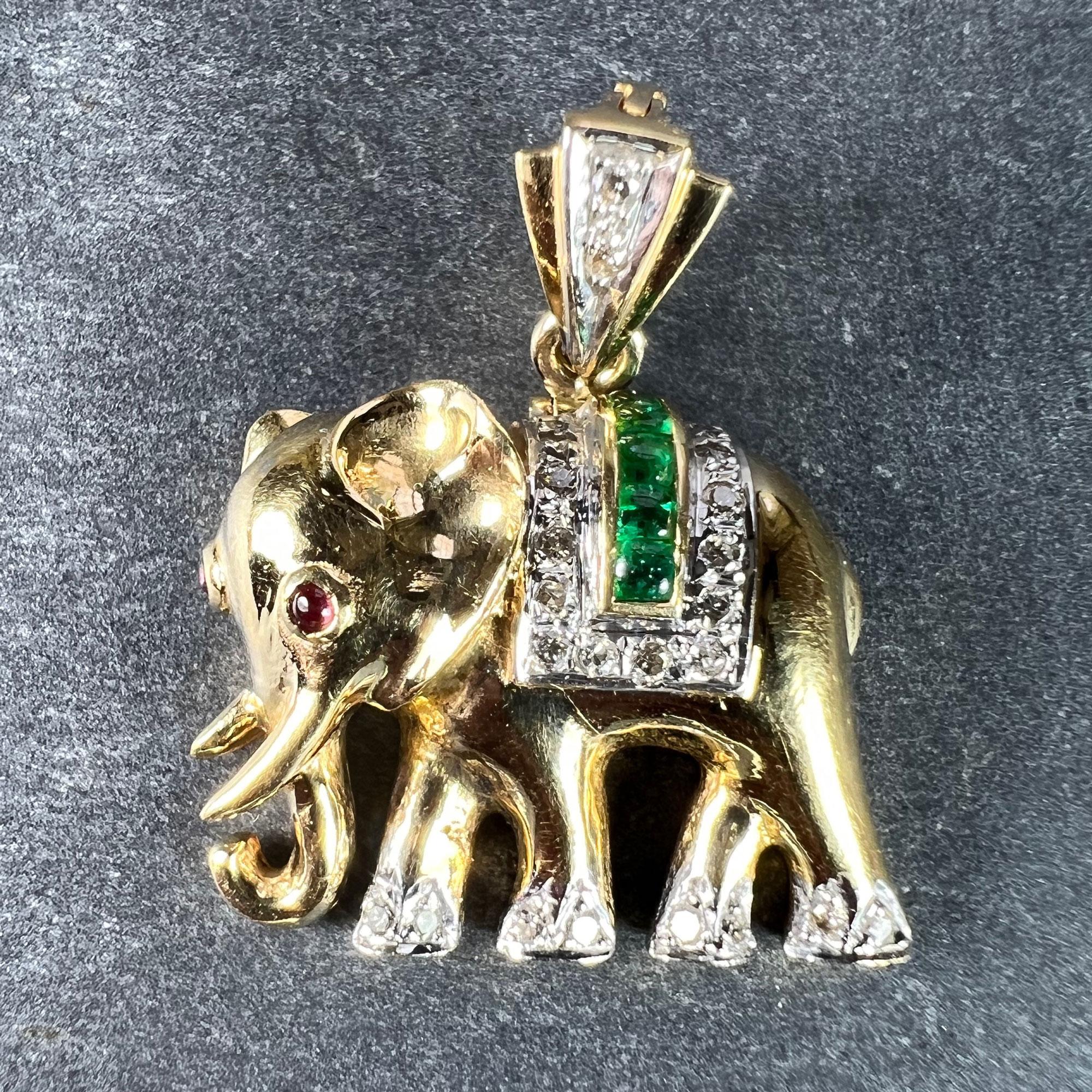 A French 18 karat (18K) yellow and white gold charm pendant designed as a lucky elephant with ruby eyes and diamond feet, with an emerald and diamond blanket over its back. The pendant bail in yellow and white gold with diamond detail. Stamped with