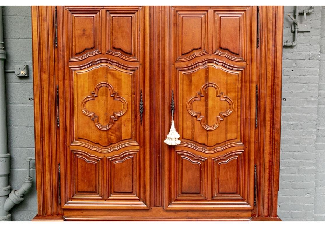 A beautifully crafted French Style Marriage Armoire. Made of exquisite honey tone wood in fruitwood stain as in the originals with an antique finish. With a tiered carved cornice over the case with multiple moldings.The double doors with carved