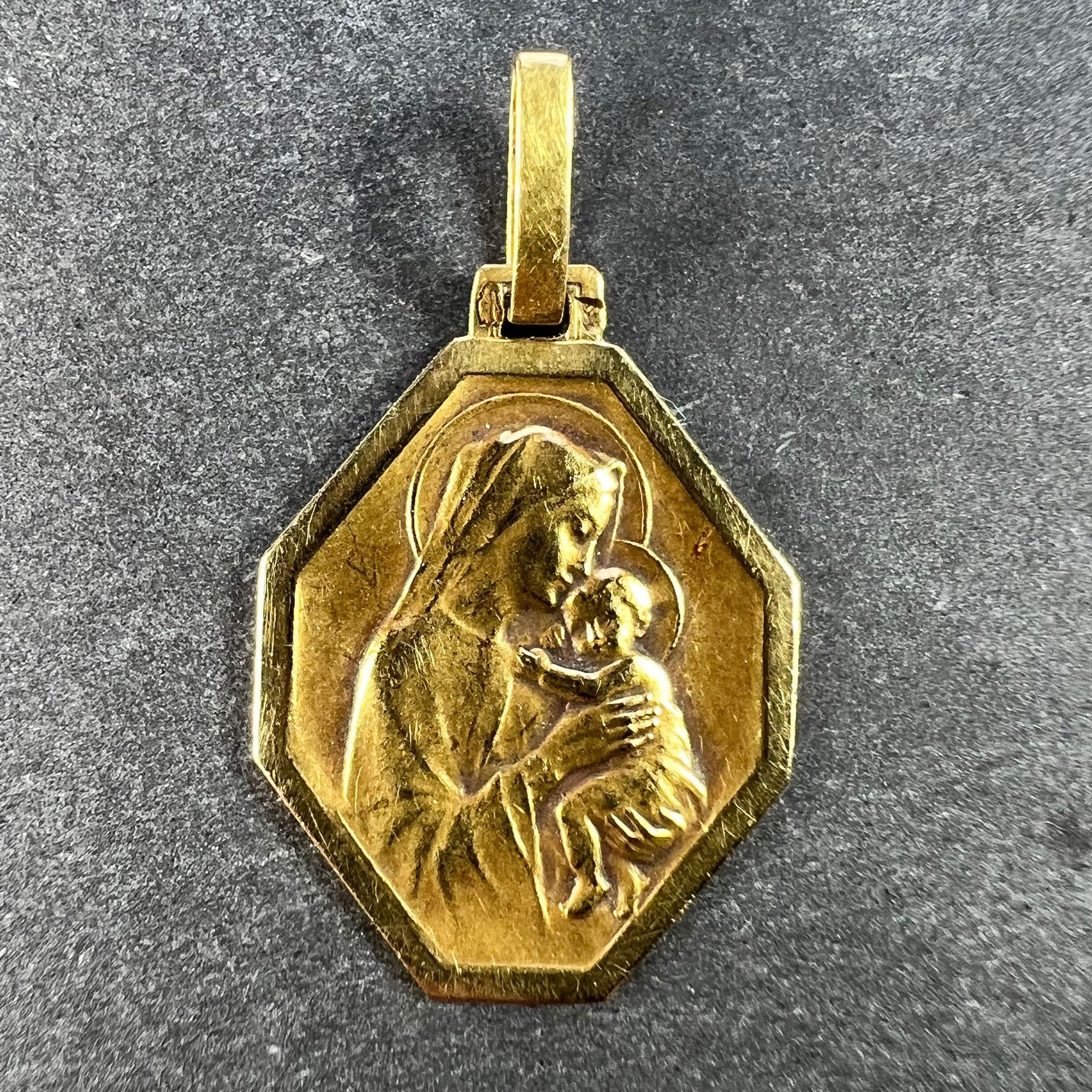 A French 18 karat (18K) yellow gold charm pendant designed as an octagonal medal depicting the Madonna and Child. The reverse is engraved with the initials MG and the date '30 Juillet 1942'. Stamped with the eagle's head mark for 18 karat gold and