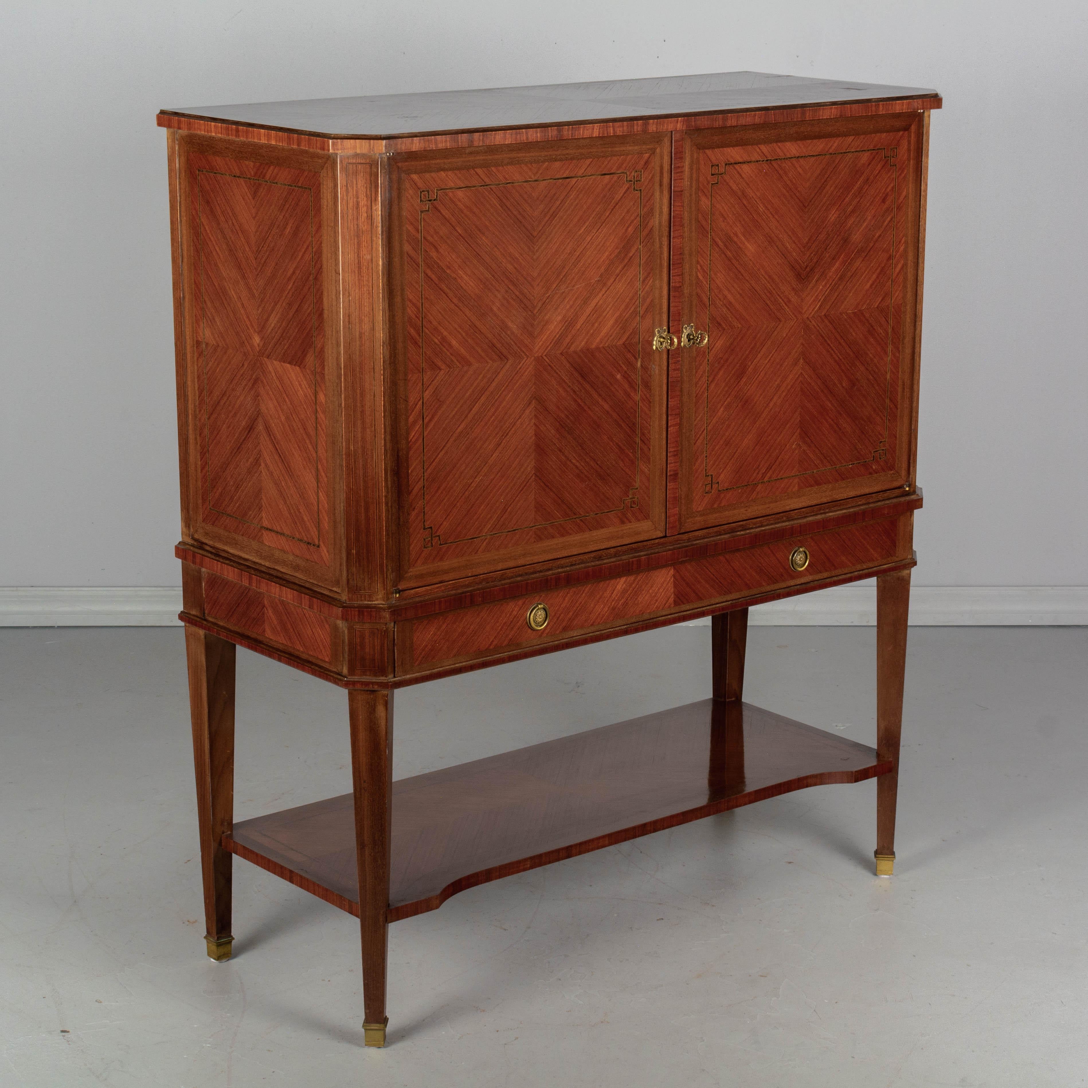 A large Louis XVI style French mahogany and rosewood bar cabinet, or buffet, with bookmatched veneers and marquetry inlay trim. Front doors with working locks and two keys. Interior has a removable shelf and provides ample storage for bottles and
