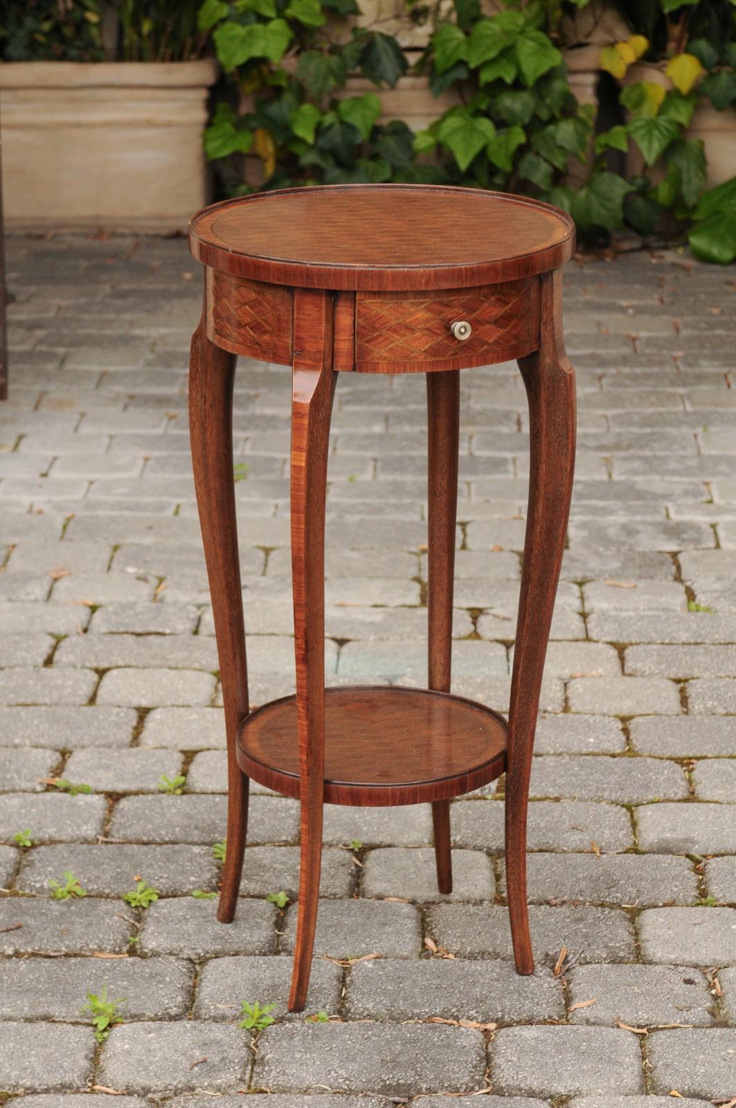 A French mahogany and walnut veneered guéridon side table from the early 20th century, with diamond motifs, single drawer, lower shelf and cabriole legs. Born in France during the Belle Époque era, this exquisite guéridon features a circular top,