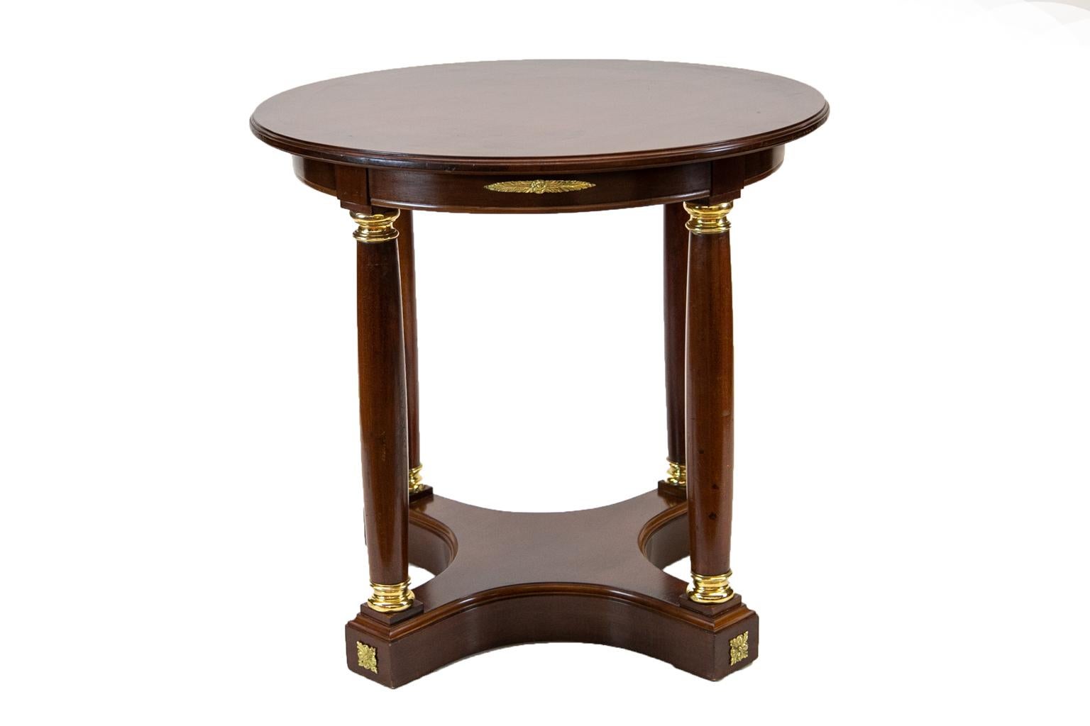 French mahogany center table, the top having a molded edge and is supported by four columns that have brass capitals and bases which terminate in a platform plinth base with concave shaping. The apron has applied brass ornamentations. The brass is